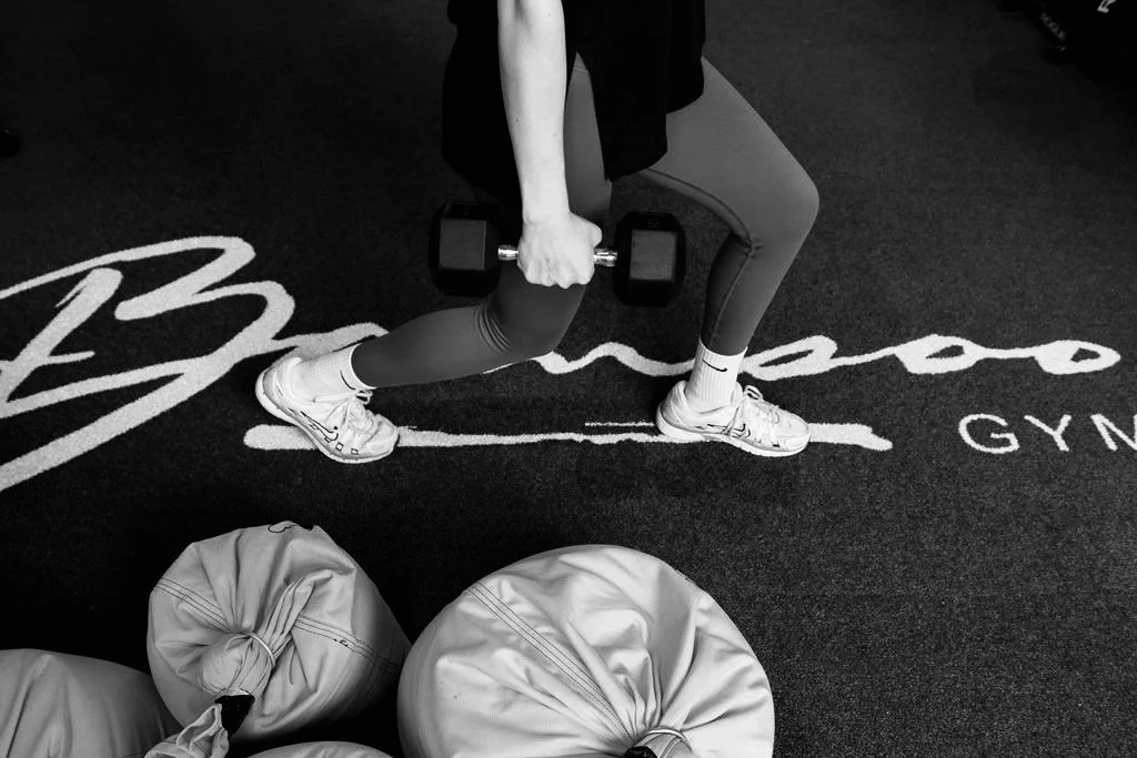 Persoon die met één knie op de grond in een sportschool gewicht tilt, met zandzakken op de vloer.