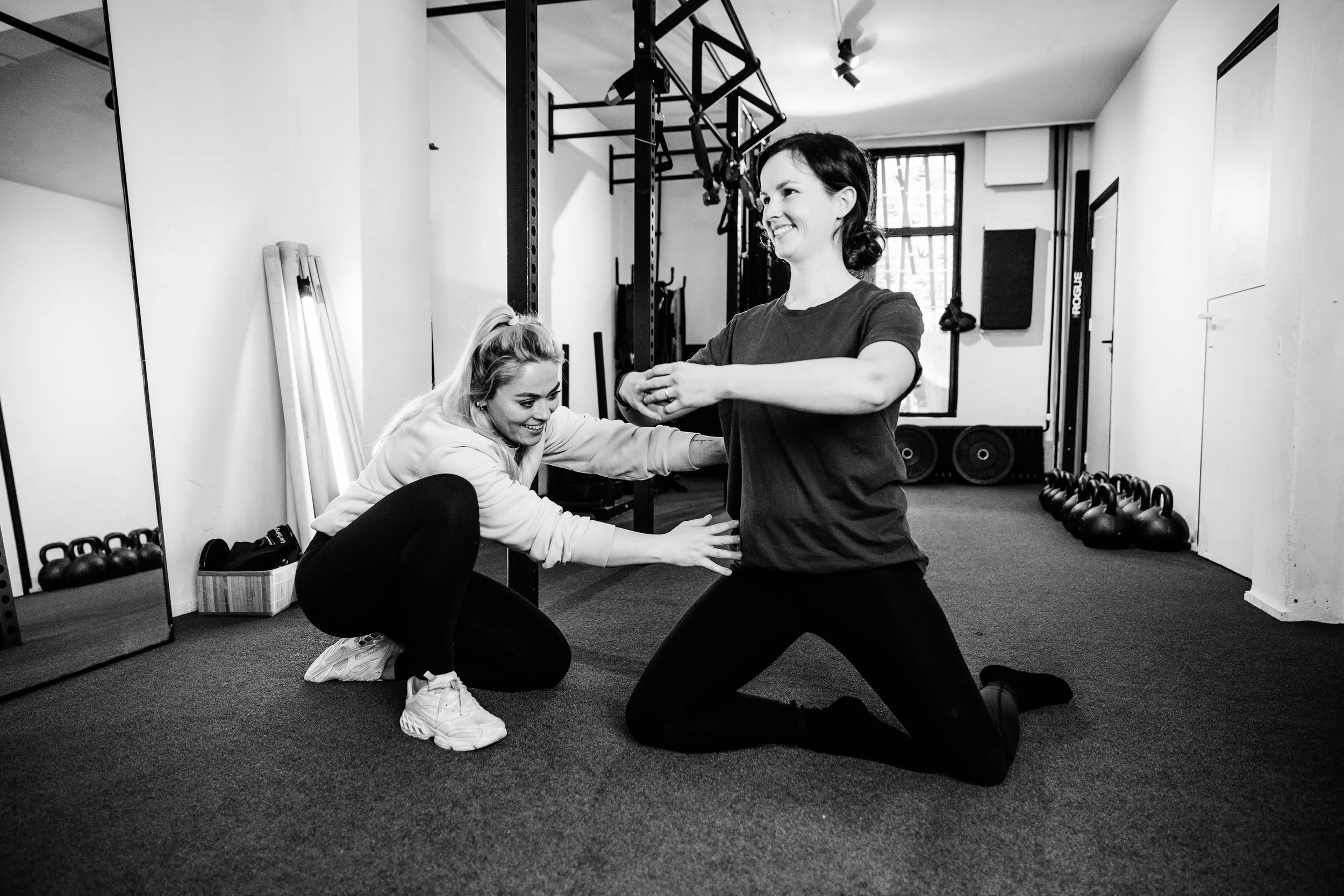 Twee vrouwen trainen in een sportschool, de ene mensen helpt de ander met oefeningen, zwart-wit foto.