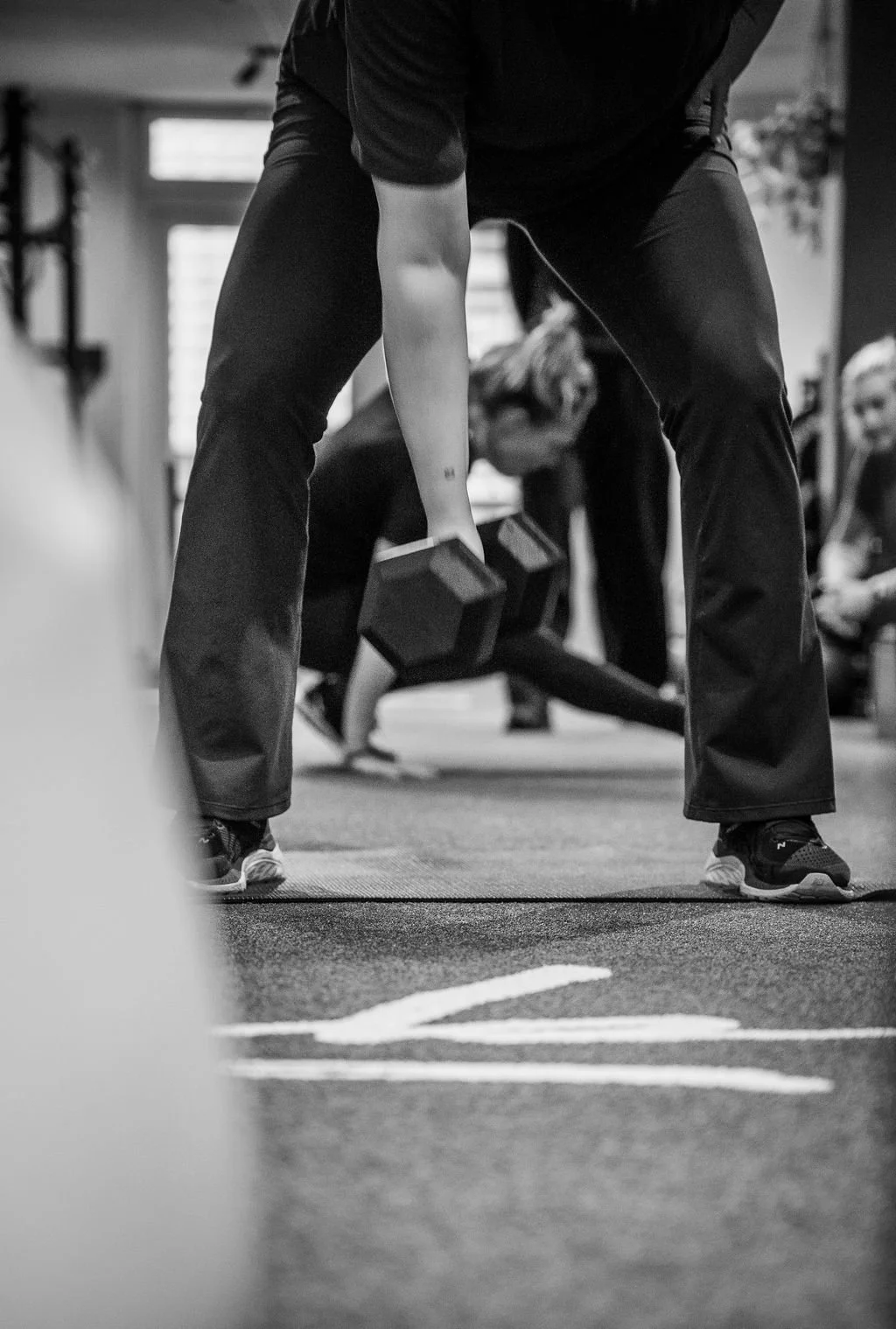 Persoon die Dukaten tilt tijdens een fitnessles, met andere mensen die aan het trainen zijn op de achtergrond, in een sportschool.