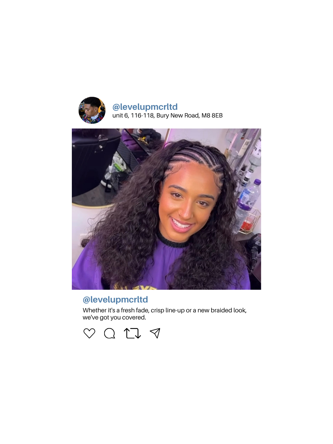 Young woman with curly hair styled with braids on top, smiling in a salon. She is wearing a purple salon cape, and hair products and tools are visible in the background.