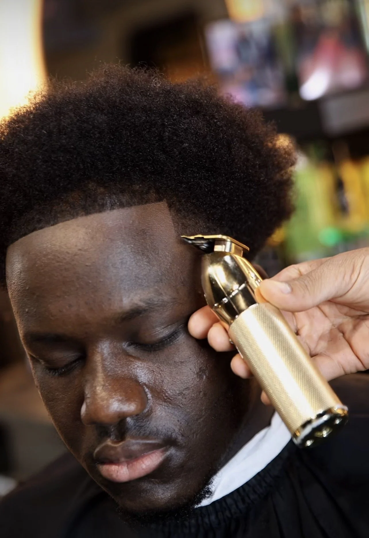 A person with closed eyes getting a haircut using an electric clippers to trim hair near the forehead.