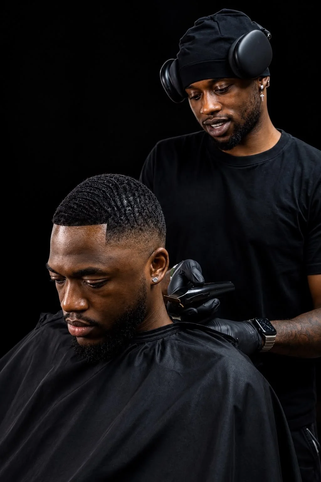 Barber giving a man a haircut with a fade hairstyle, with a black background.