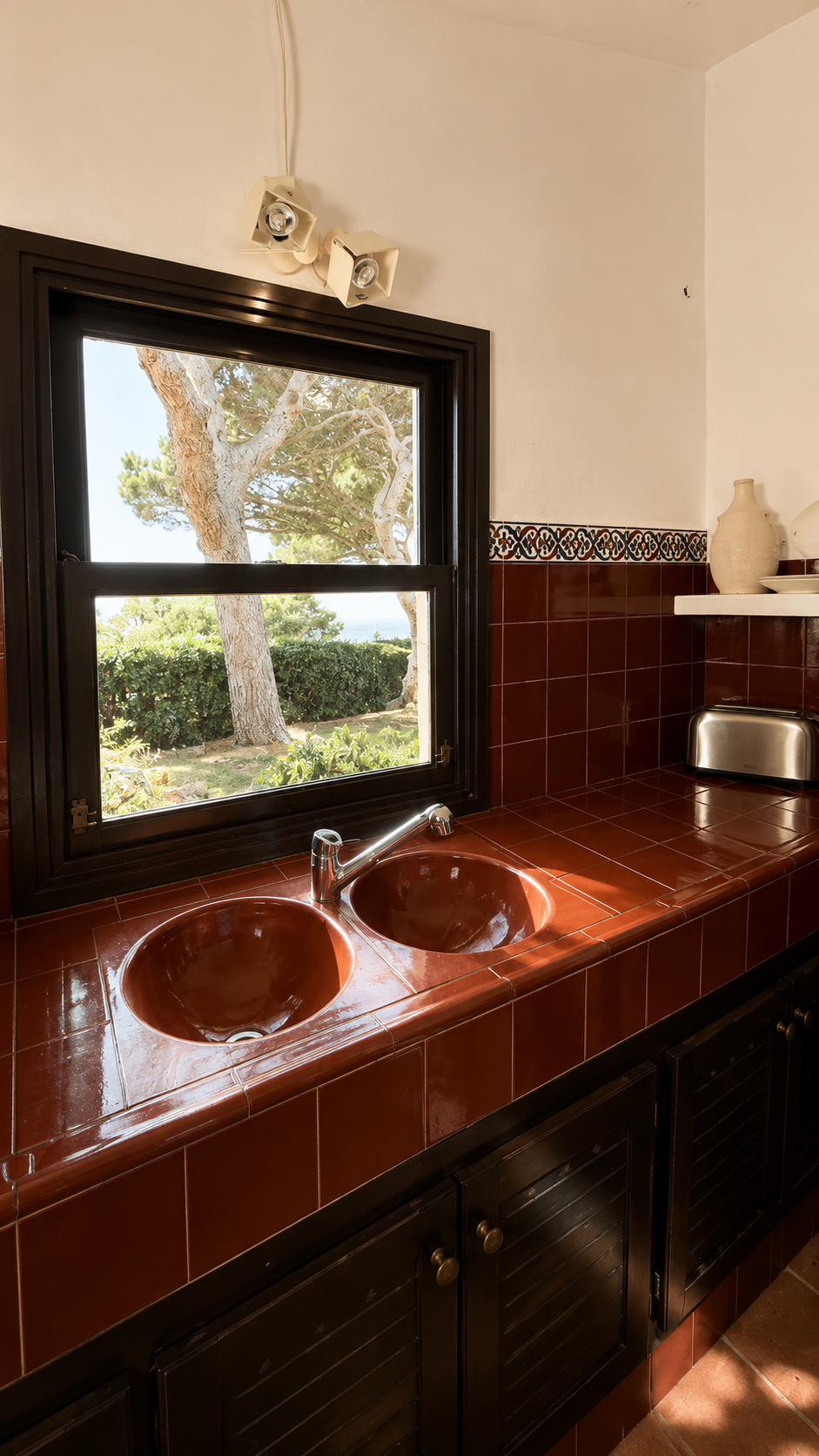 Lavabo de cerámica en una cocina con ventana que muestra árboles y plantas afuera.