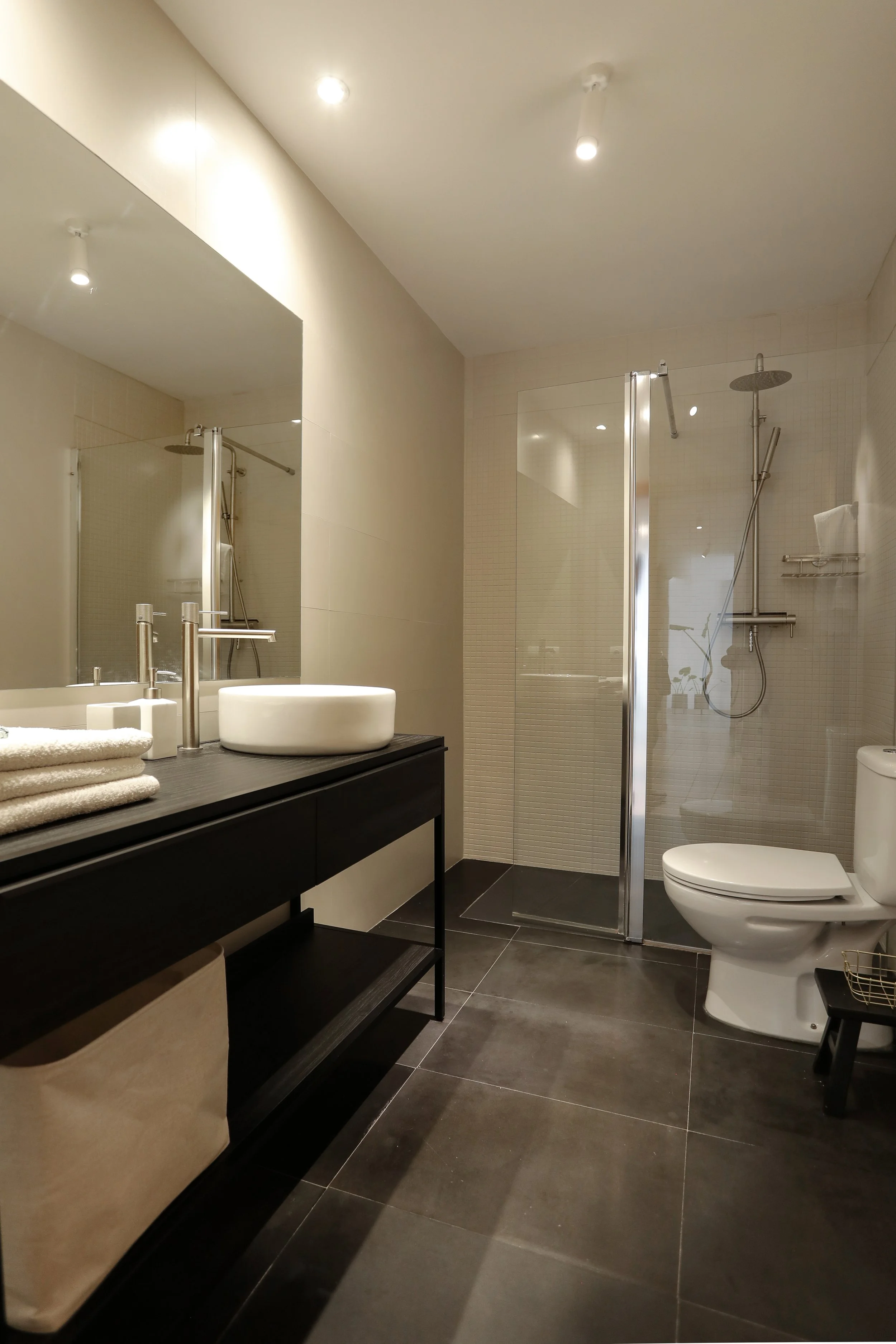 Baño moderno con ducha de cristal, lavabo sobre una repisa negra y toallas dobladas.