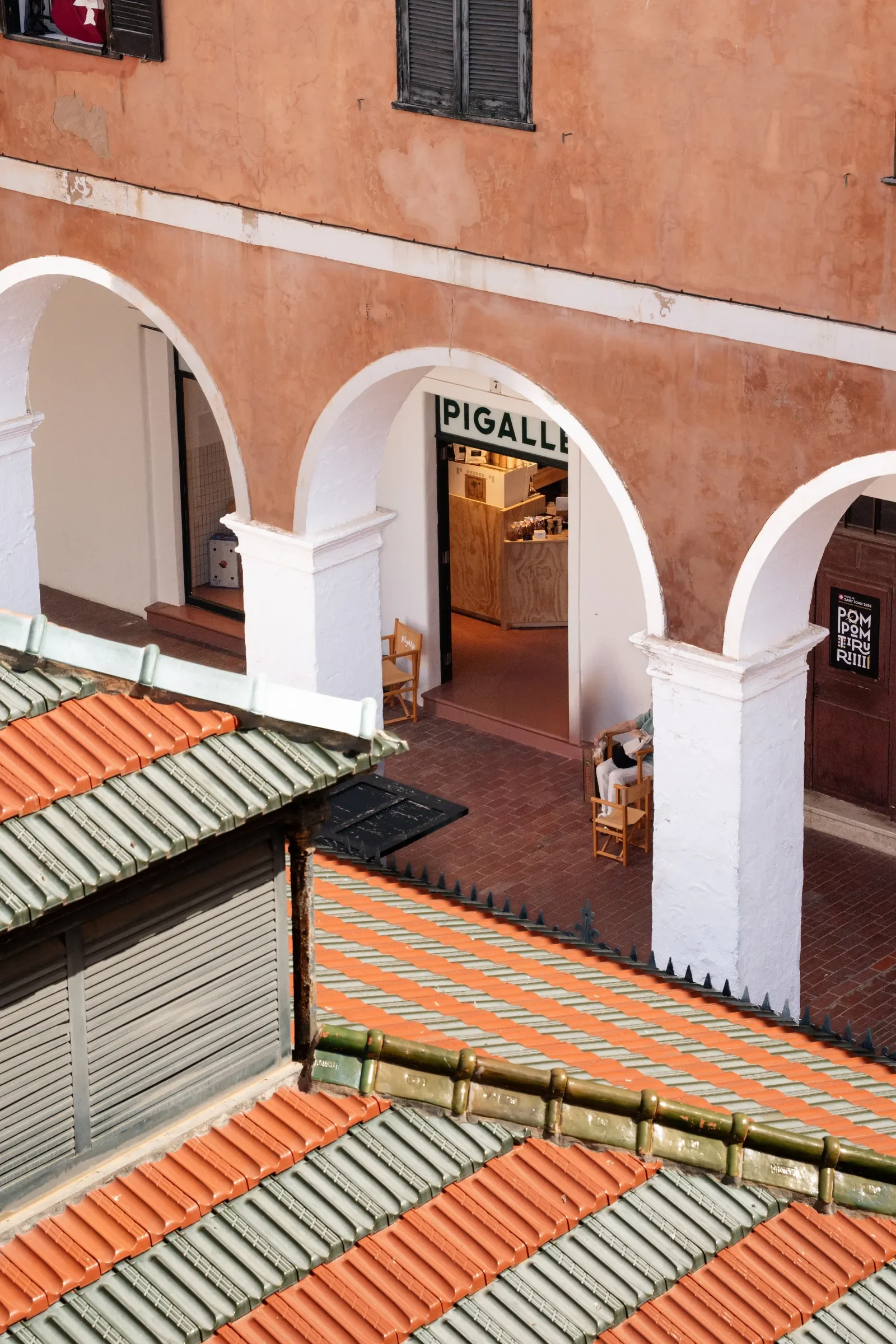 Vista desde arriba de un edificio con paredes de color terracota y arcos blancos, además de techos de tejas en colores rojo y verde, en un entorno urbano.