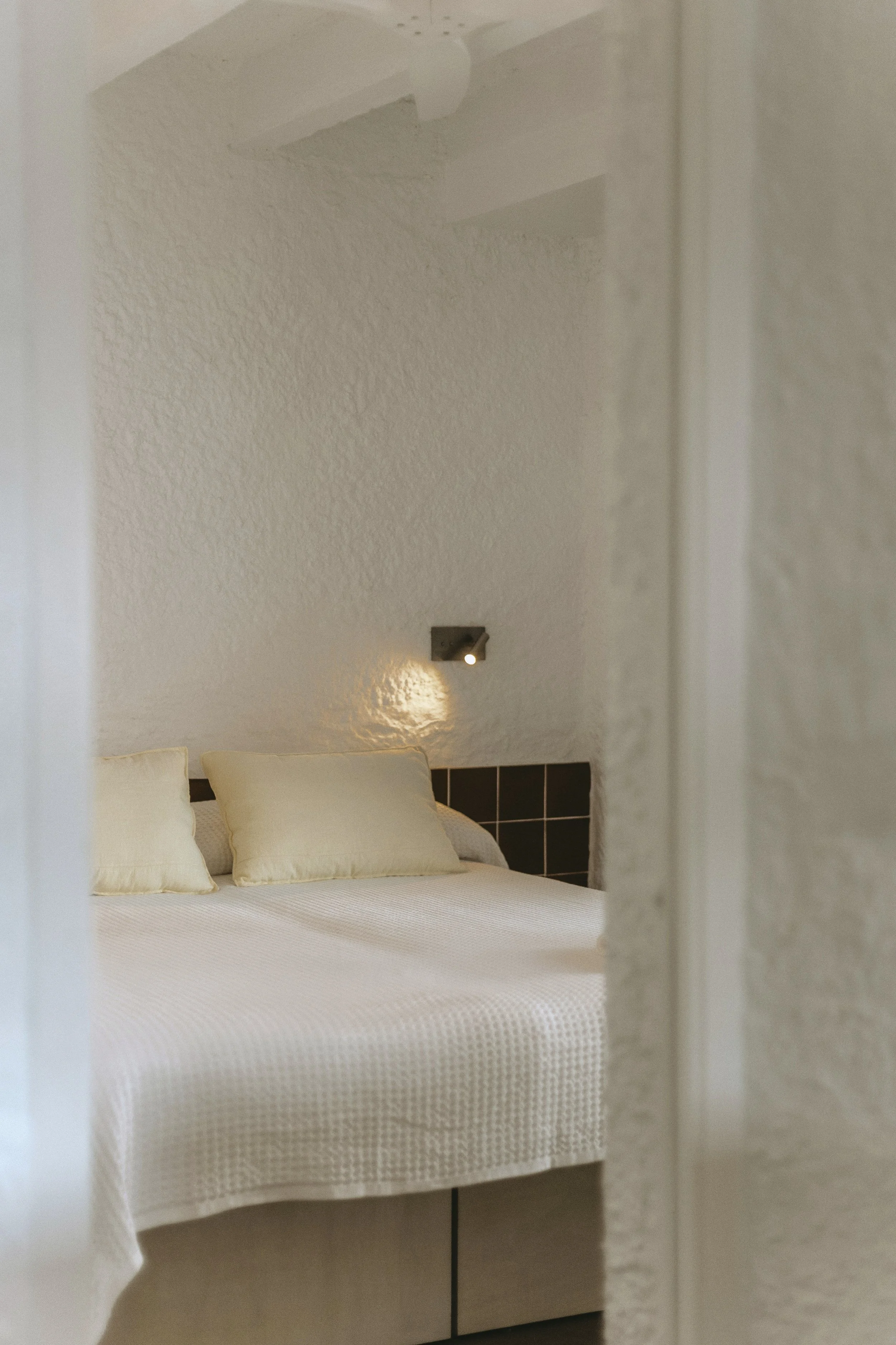 Cama con almohadas claras en una habitación con paredes blancas y una lámpara de lectura
