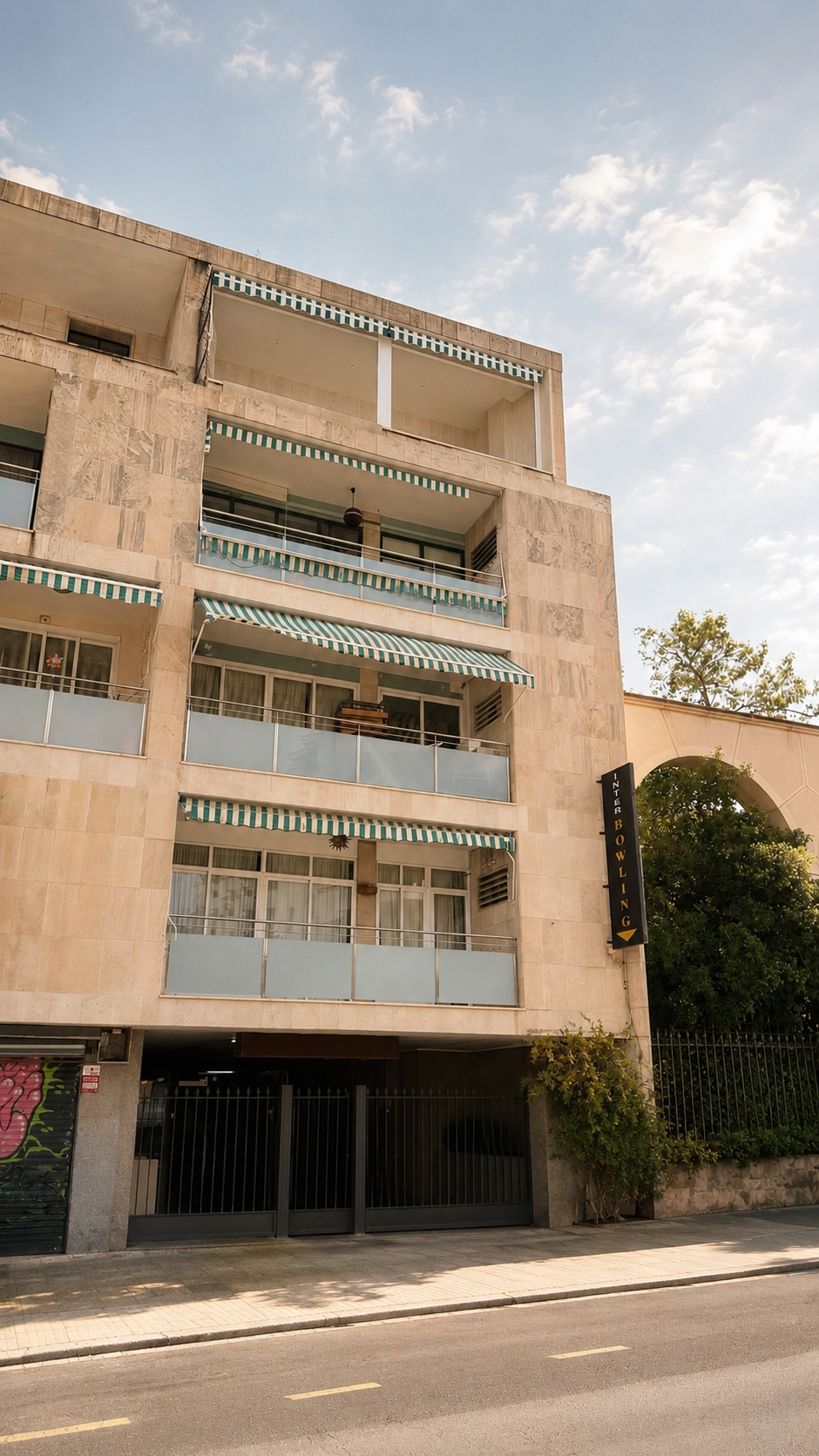 Edificio de varios pisos con balcones y toldos azules y blancos, cartel que dice 'INTER BOWLING', puertas de entrada con rejas y un árbol a la derecha.