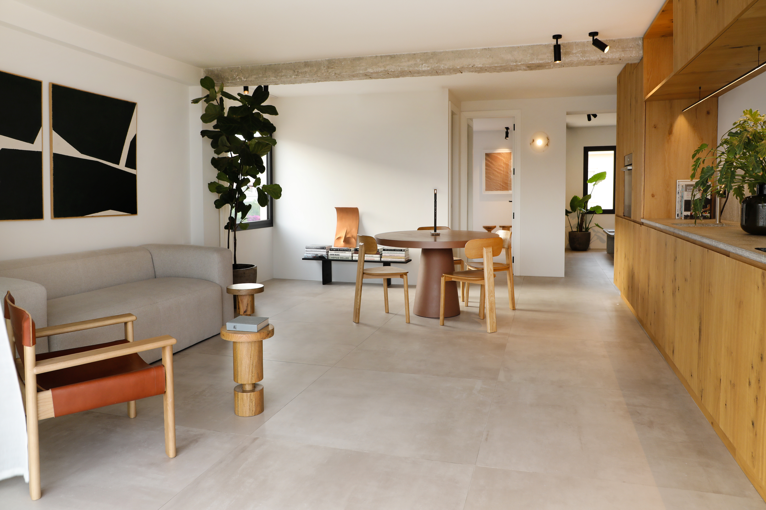 Sala de estar moderna con muebles de madera, sillones y plantas decorativas, paredes blancas y arte abstracto colgado.