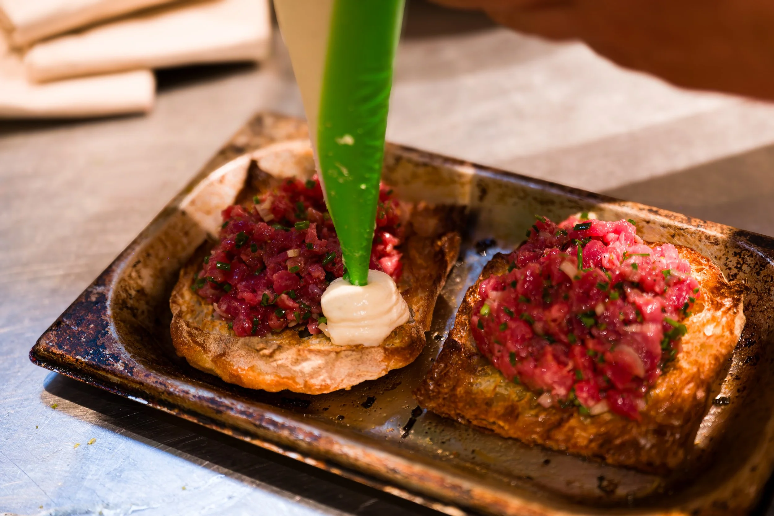 Twee stukjes toast met tartaar, afgewerkt met een groene blad, een beetje saus, en fijngehakte groen