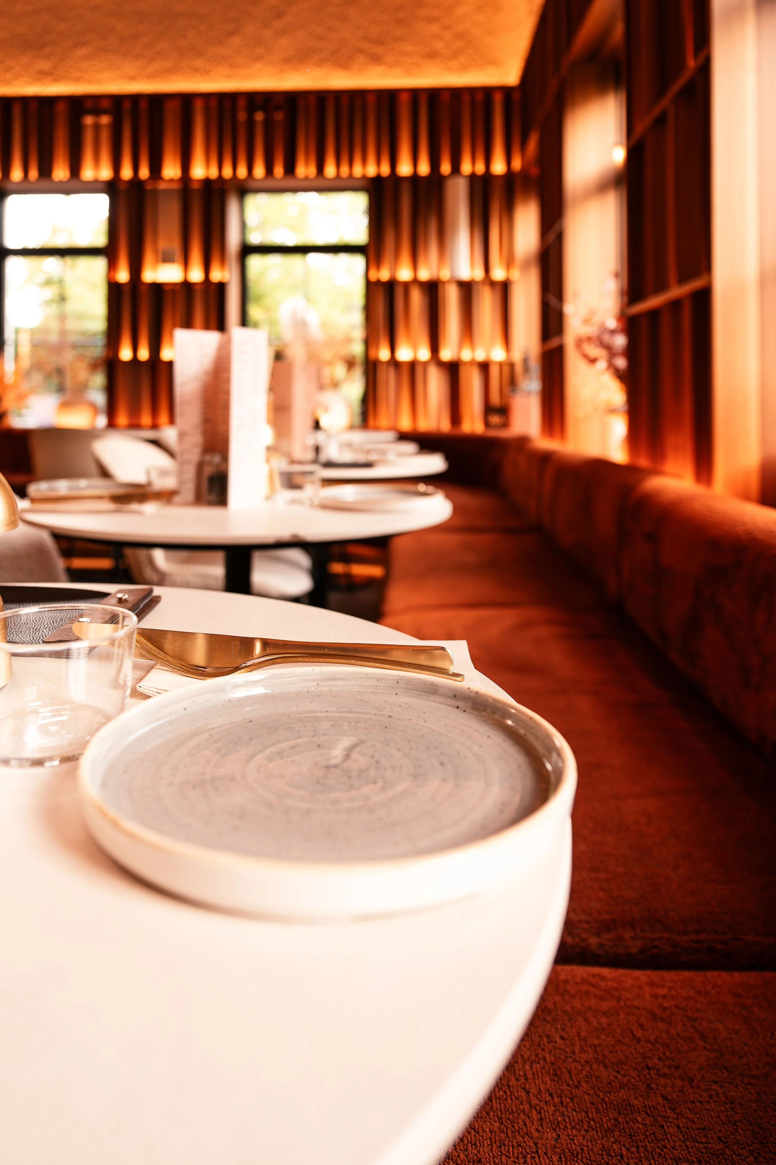 Een restaurantinterieur met houten wanden, ramen en gedekte tafels met keramische borden, bestek en glazen.