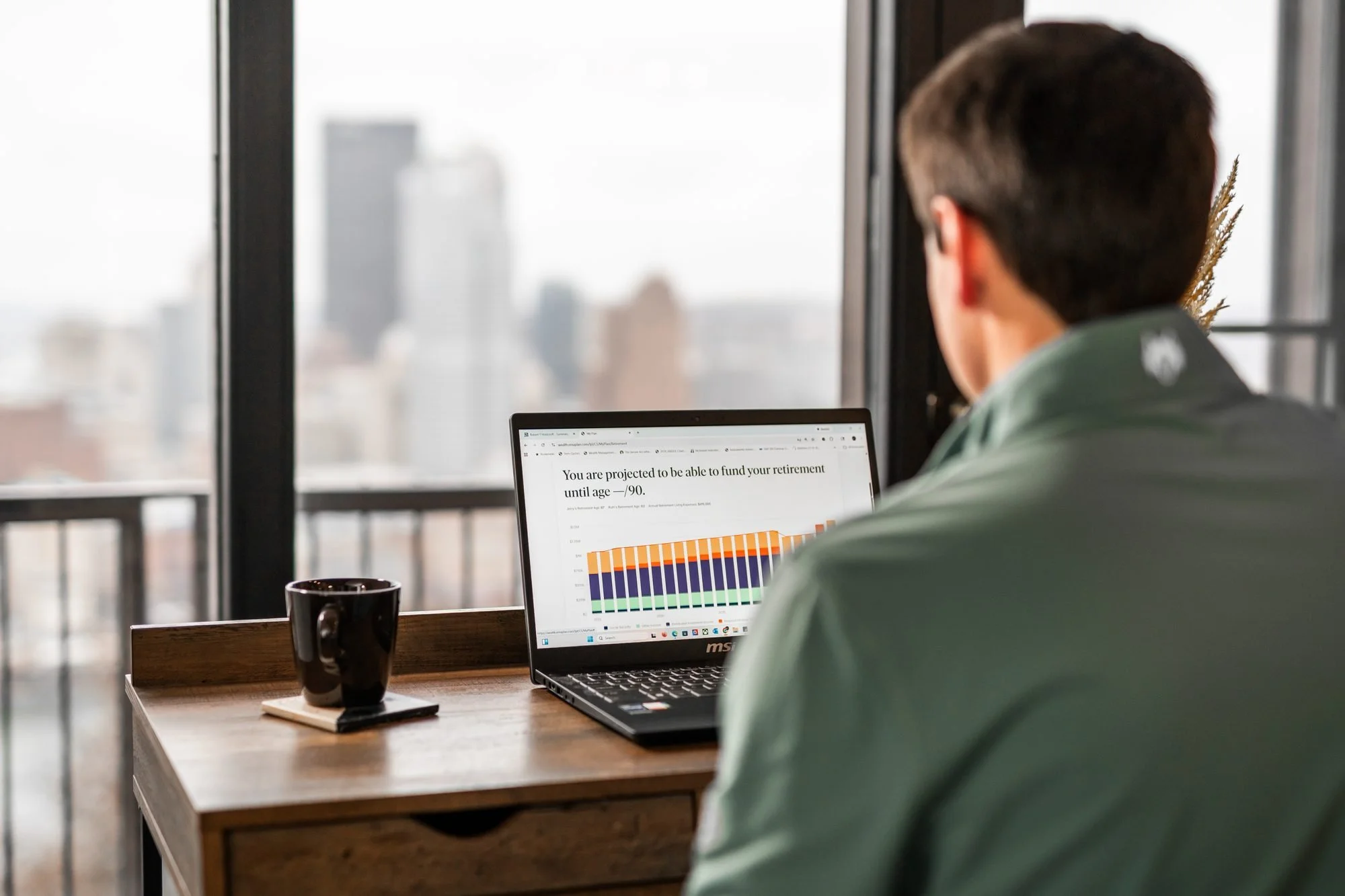 Rob Holdcroft reviewing a financial plan at his desk overlooking downtown Pittsburgh