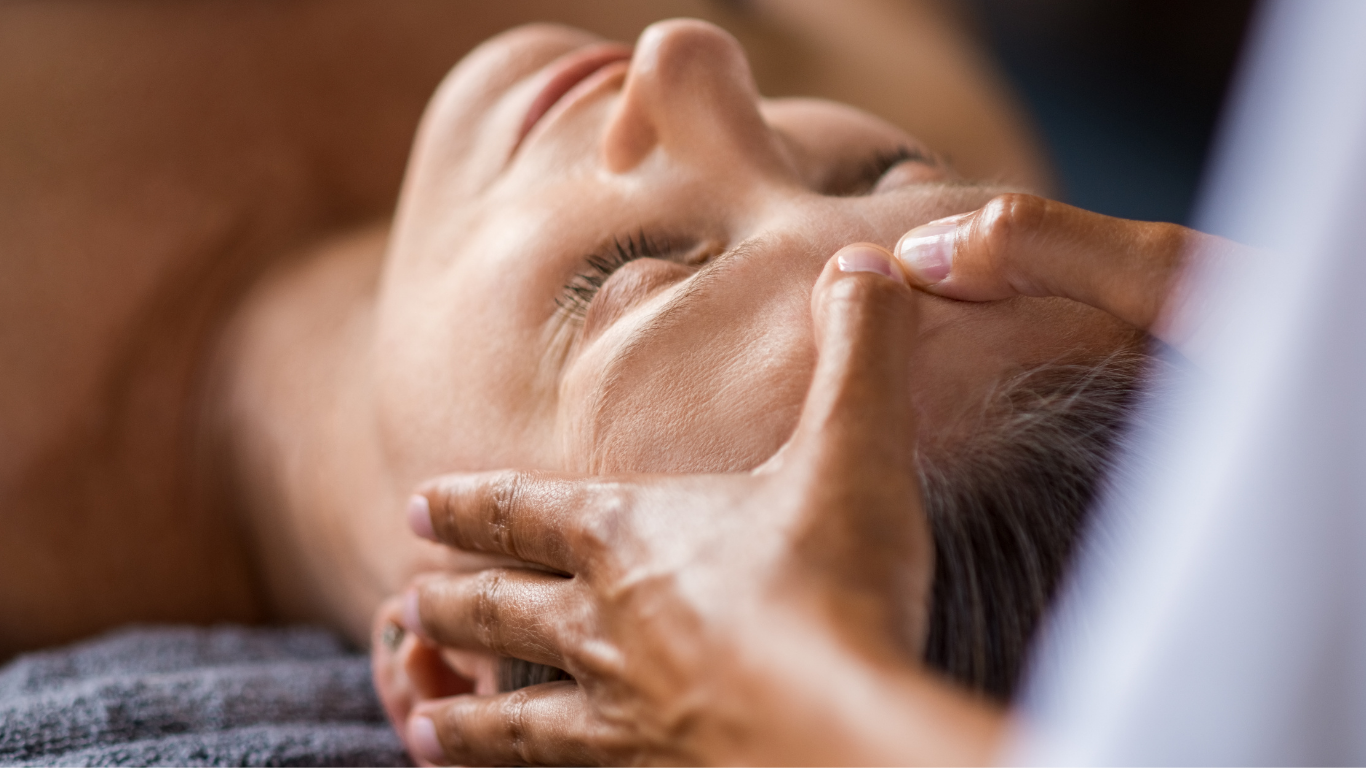 A woman receiving a facial massage from a skincare professional in a spa or clinic setting.
