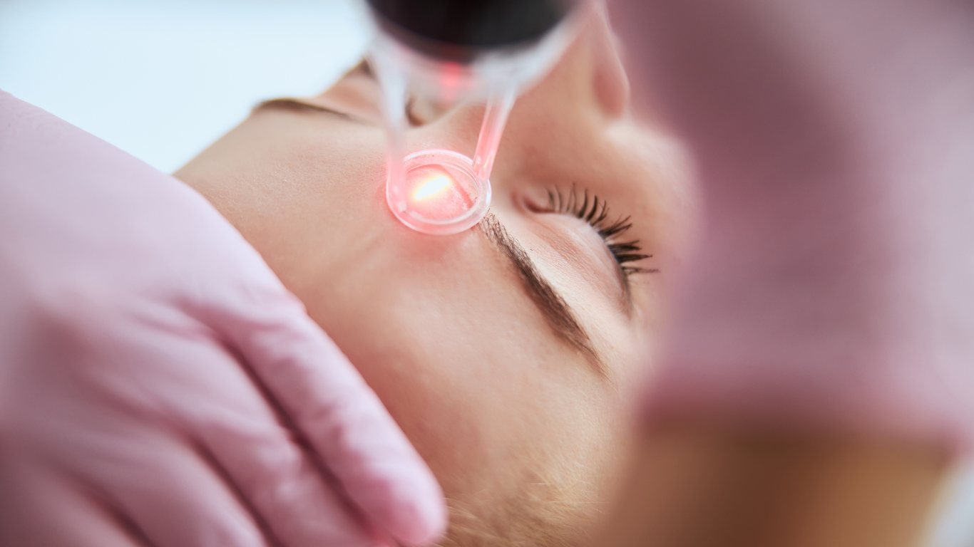 Person receiving a facial laser treatment emitting red light on their face.