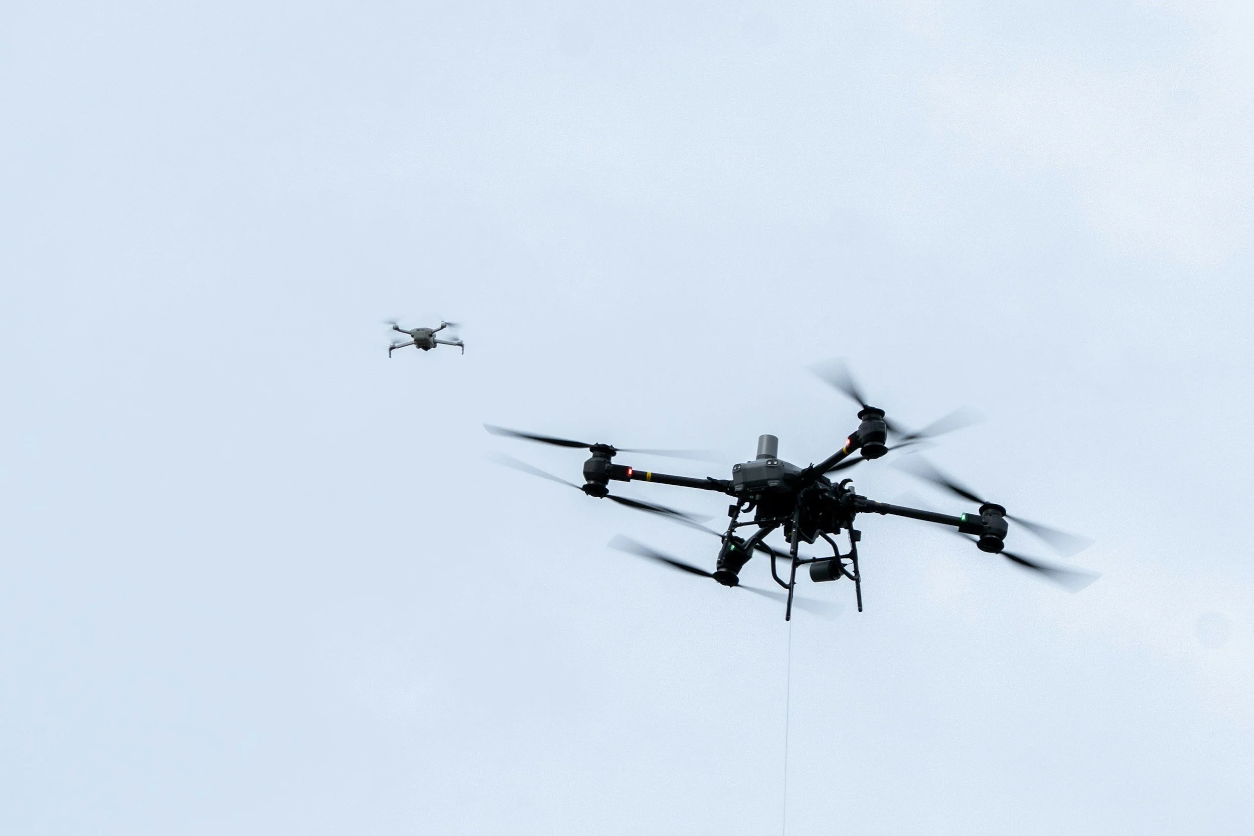 A large quadcopter drone in flight with two smaller drones flying nearby against a cloudy sky.