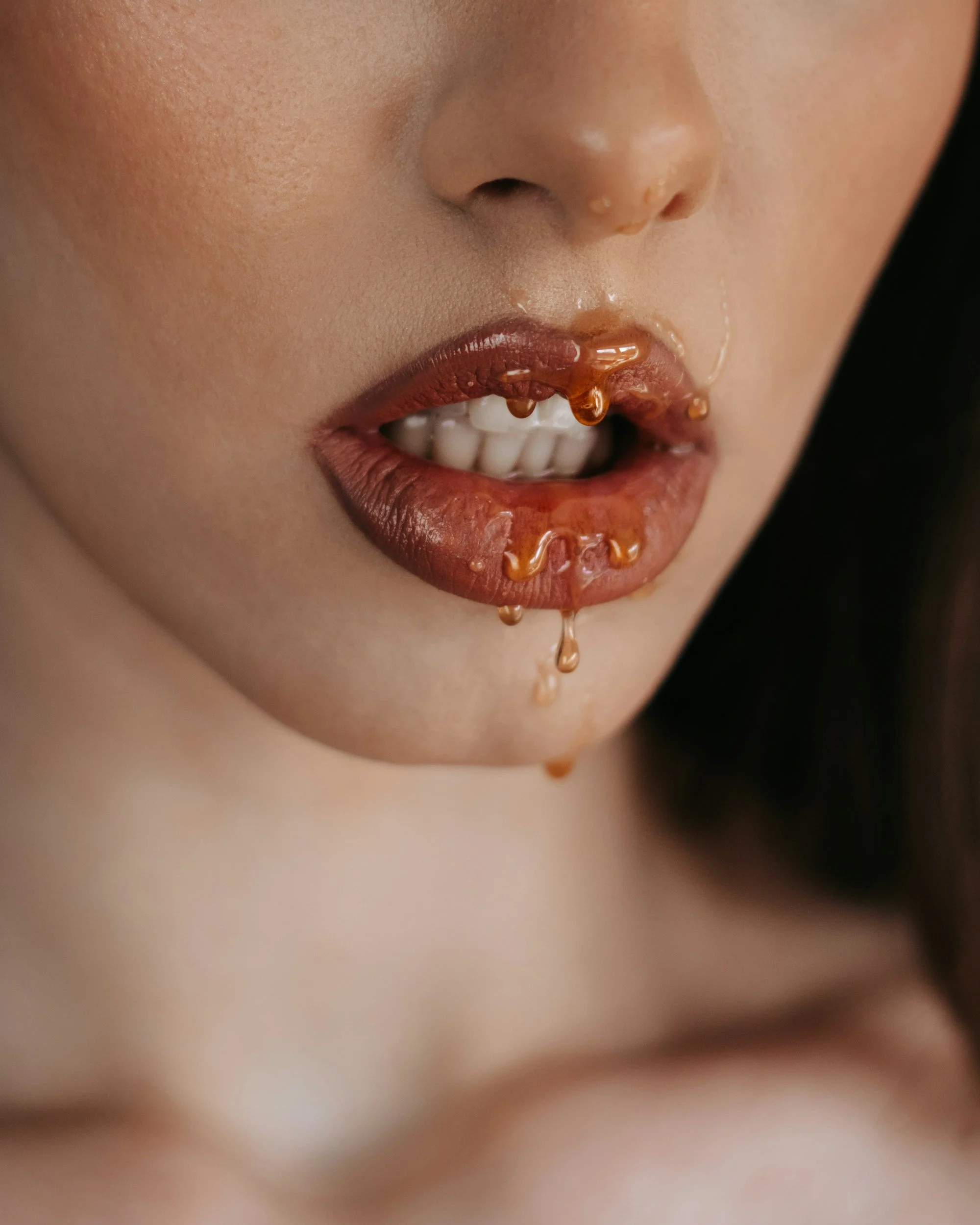 Close-up of a person's face with lips slightly parted, showing some saliva around the mouth, and a blurred background.