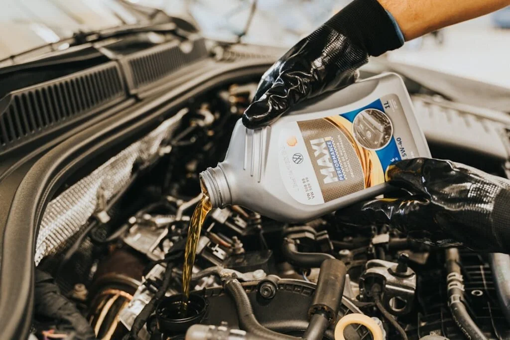 Person pouring motor oil into a car engine using a bottle labeled 'VAN' with black gloves on.