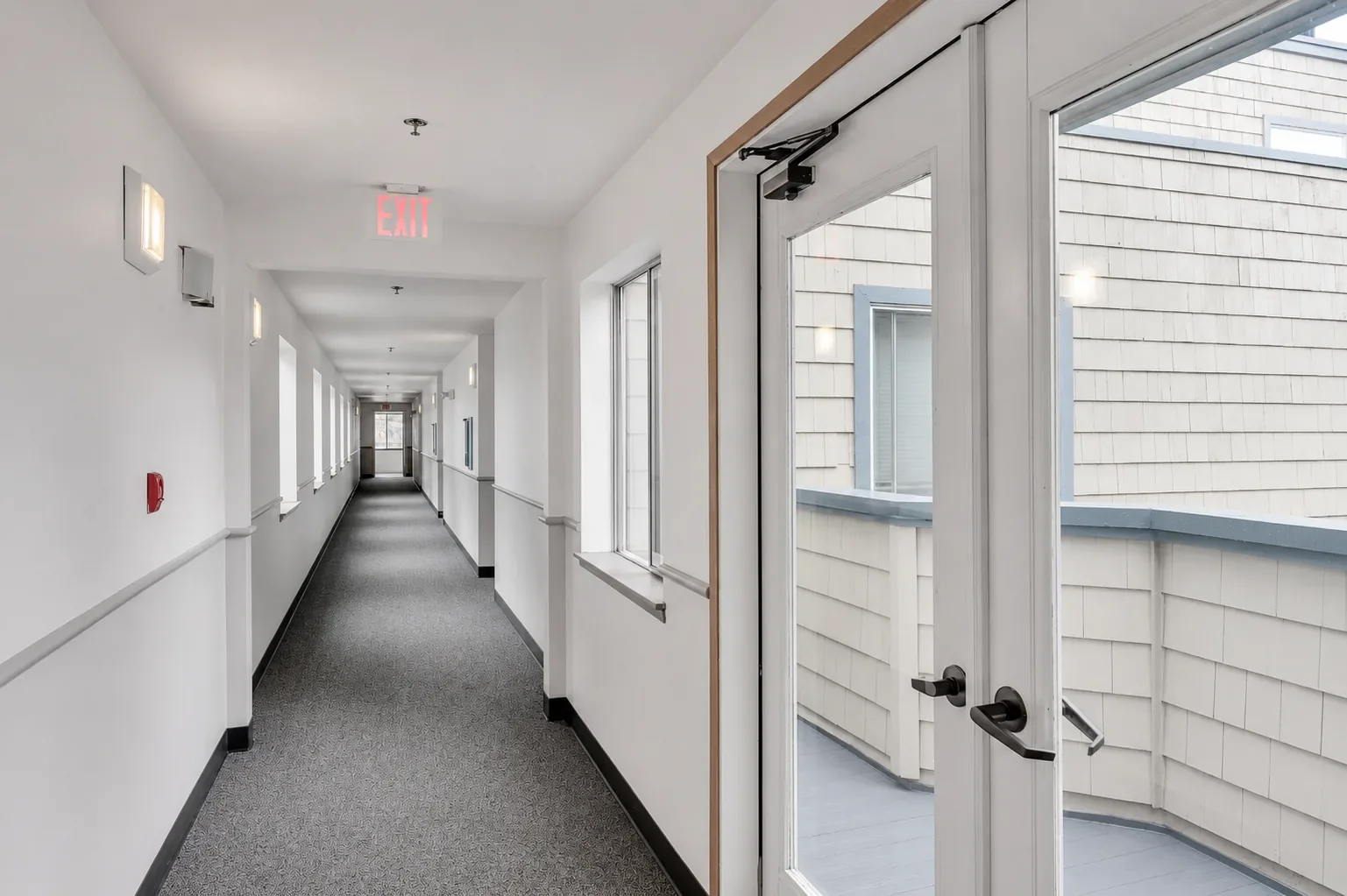 Empty indoor corridor with white walls, black trim, and exterior door leading to a balcony or terrace.