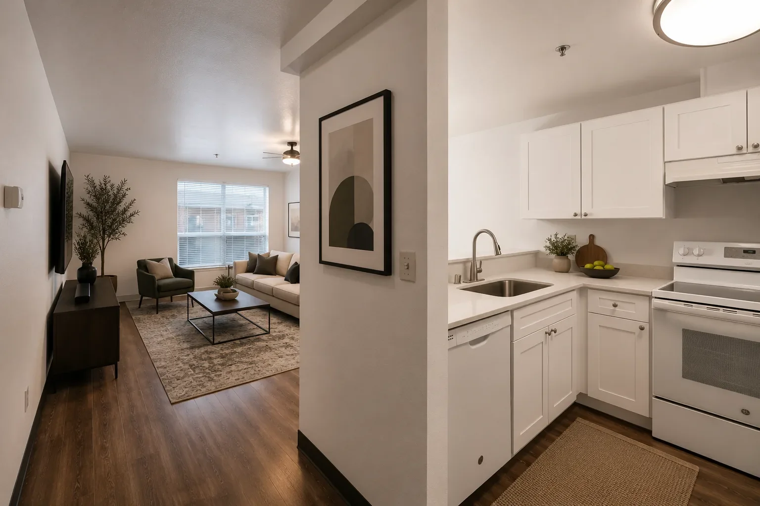 Living room with window and sofa, adjacent kitchen with white cabinets and appliances.
