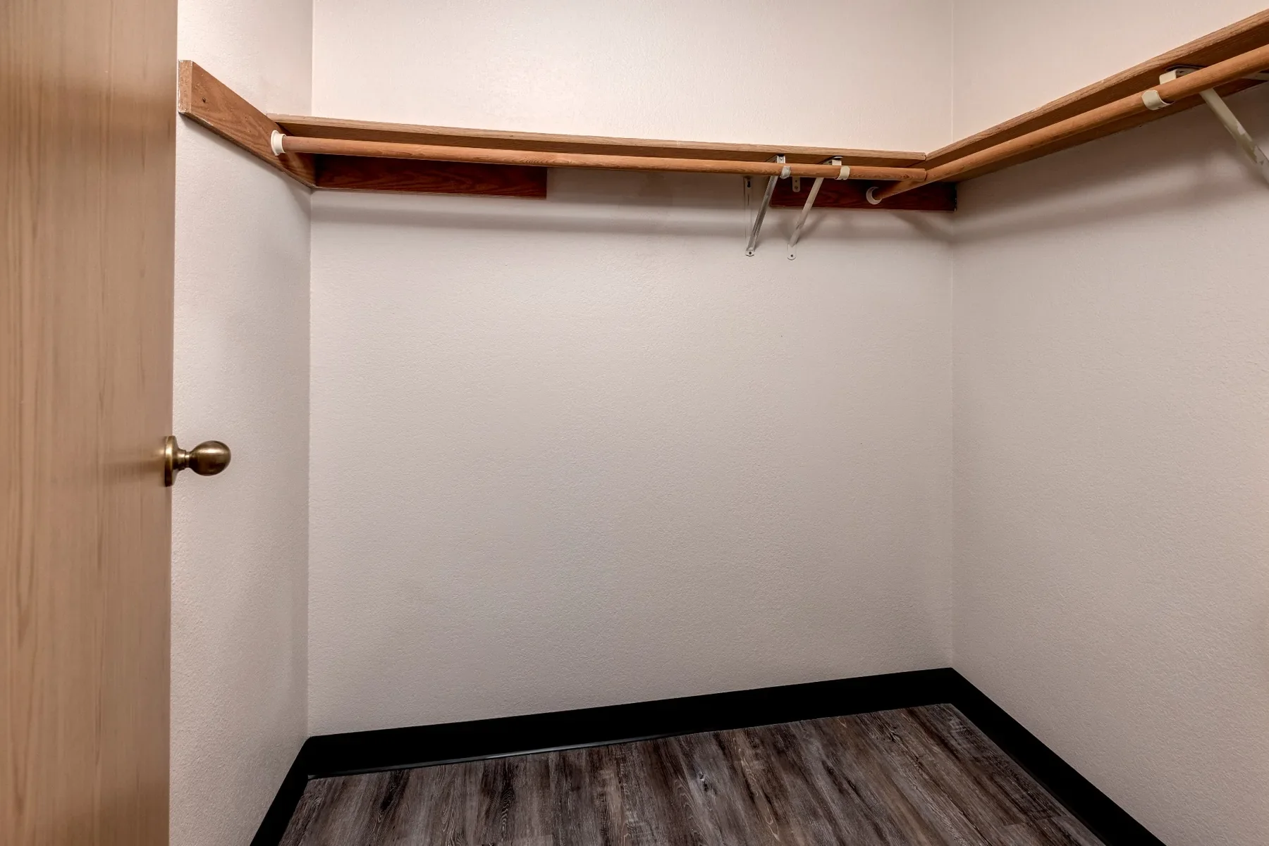 Empty walk-in closet with wood shelf, hanging rod, and dark wood laminate flooring.