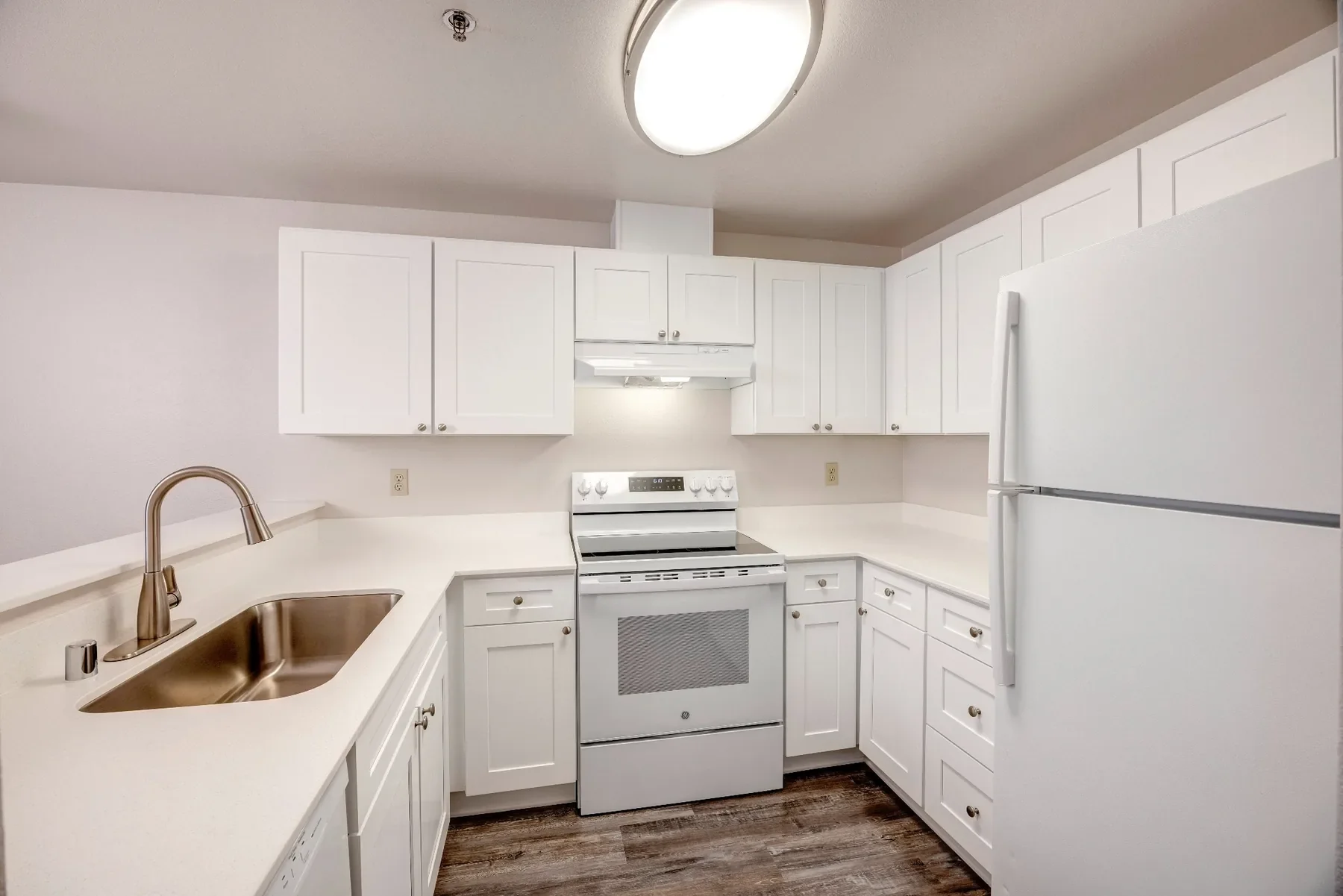 A kitchen with white cabinets, a white stove, a white refrigerator, a beige countertop with a sink, and a ceiling light fixture.