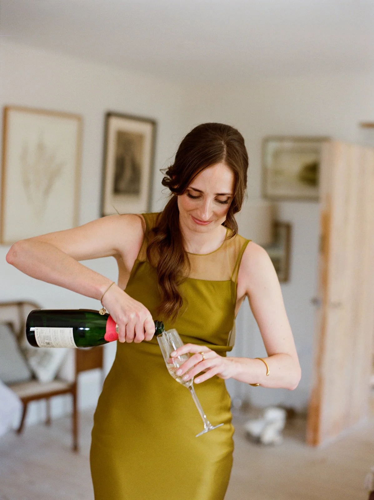 A woman in a yellow dress pouring champagne into a flute glass indoors.