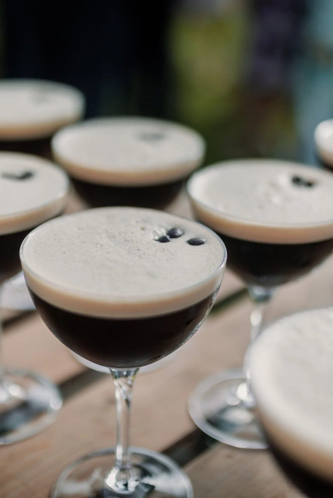 Multiple glasses of a dark cocktail topped with whipped cream and garnished with coffee beans, arranged on a table.