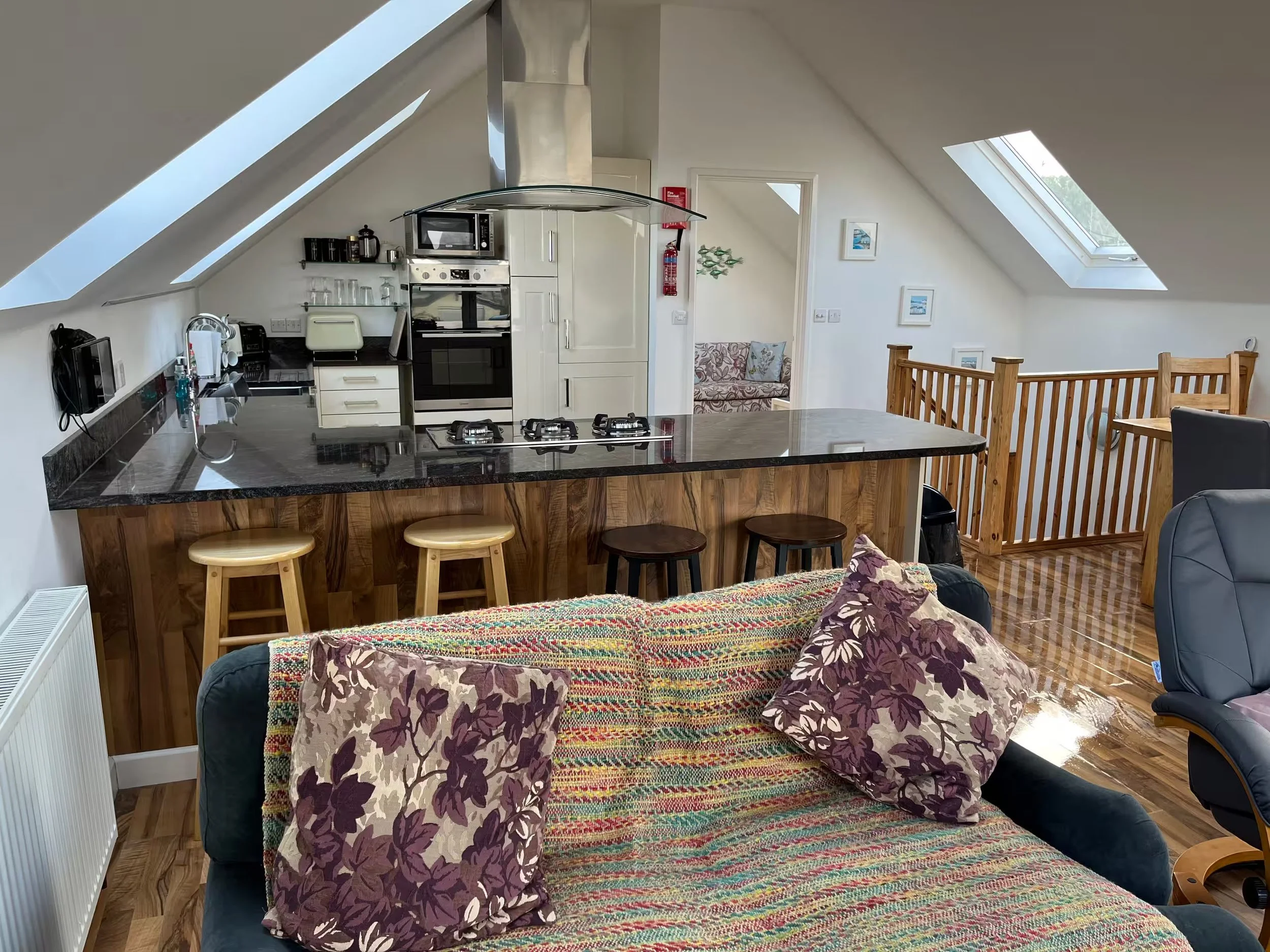 Interior of Sunnyridge with a kitchen, bar stool seating, a sofa with floral pillows, and skylight windows on the sloped ceiling.