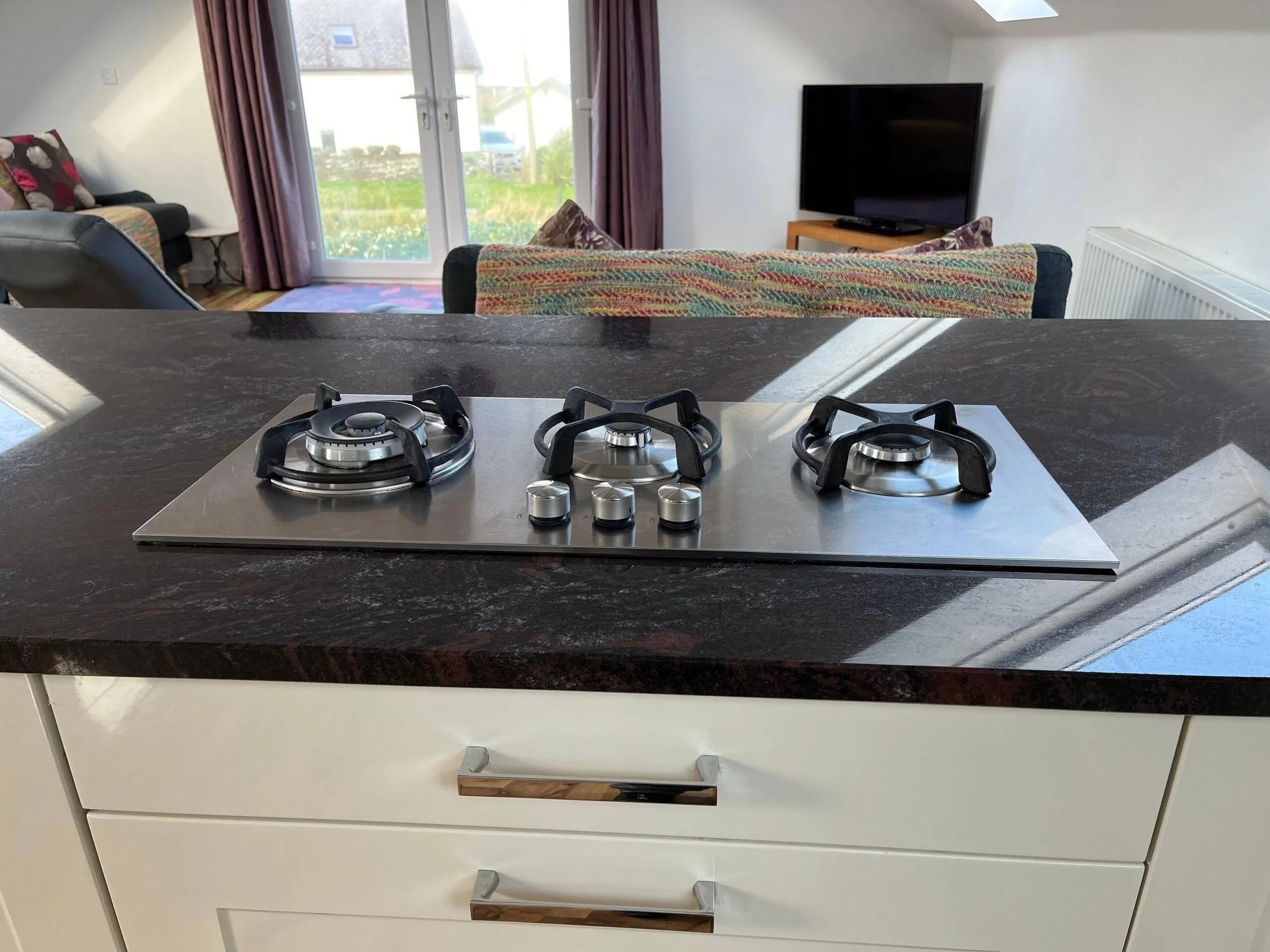 Kitchen counter with black granite surface and three gas burners, view from above, with white cabinetry below.