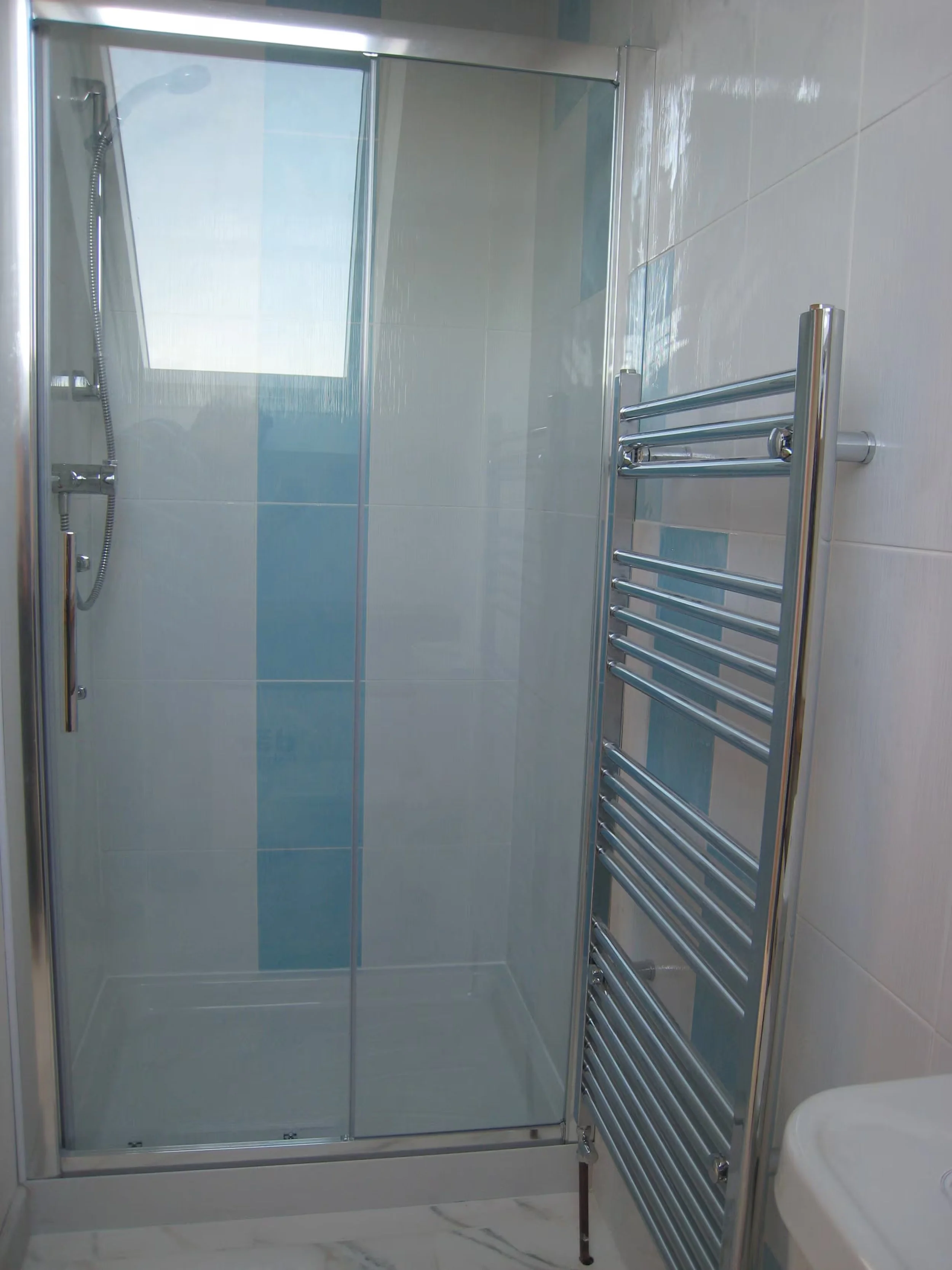 Upstairs showerroom at Sunnyridge with a glass-door shower enclosure, a towel rail on the wall, and a partial view of a white sink and marble flooring.