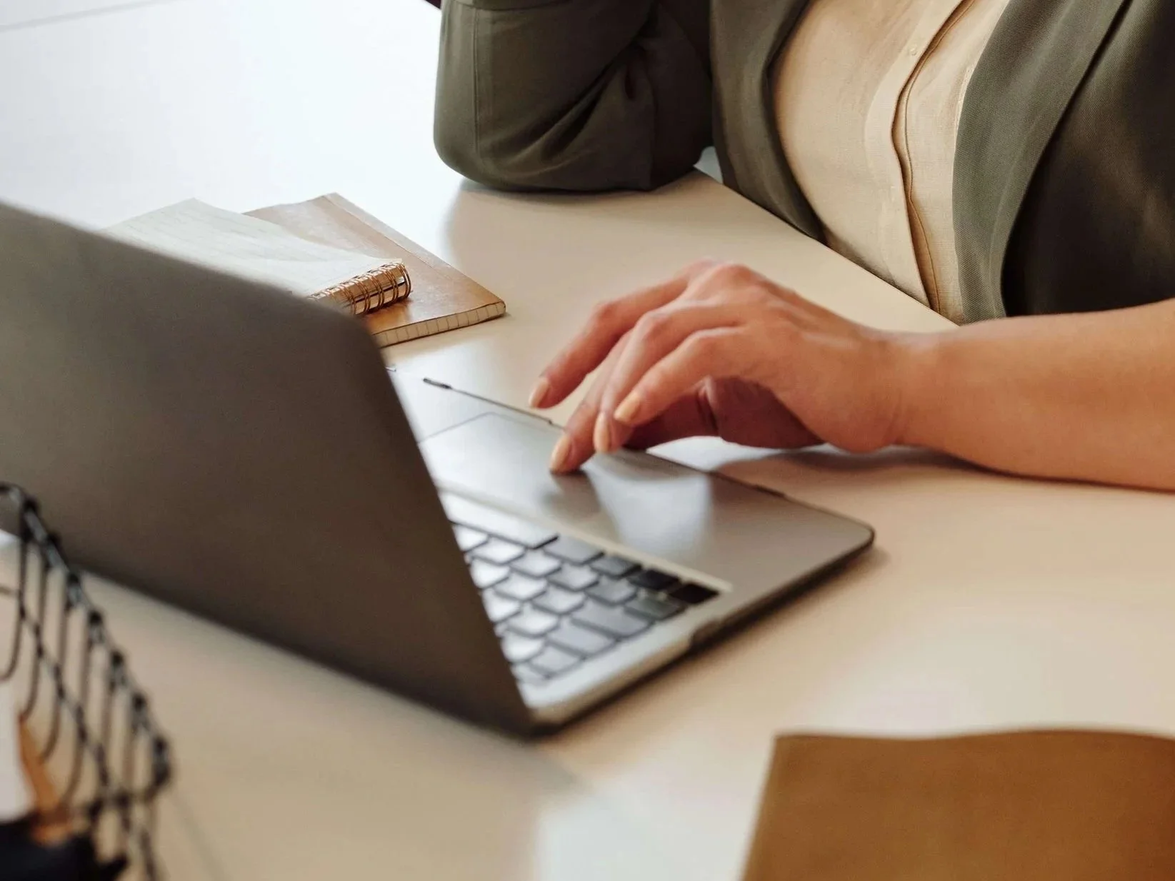 Person using a laptop at a desk, with a small notebook and another notepad nearby.