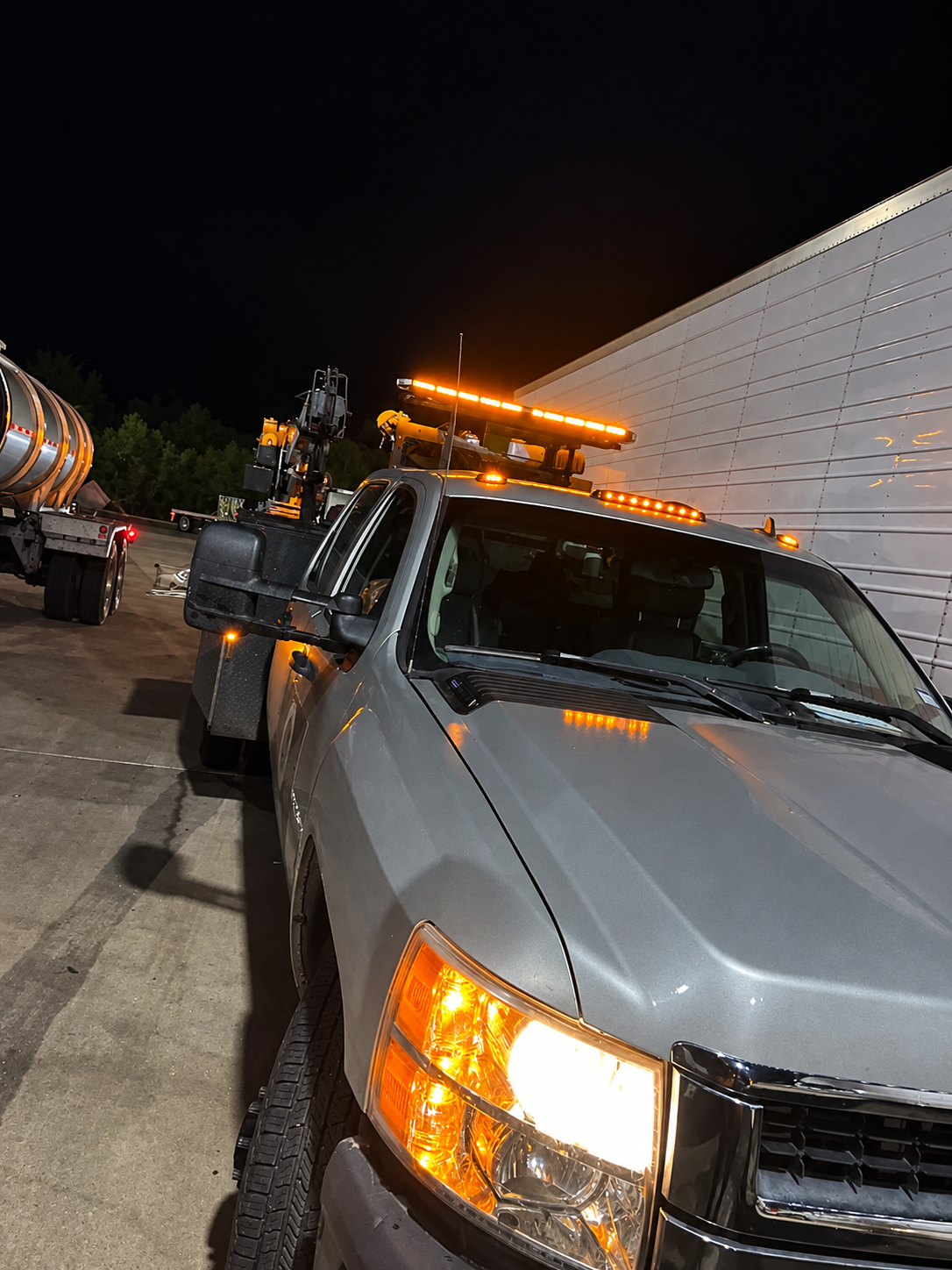 Service truck with amber warning lights illuminated beside a semi-trailer at night.