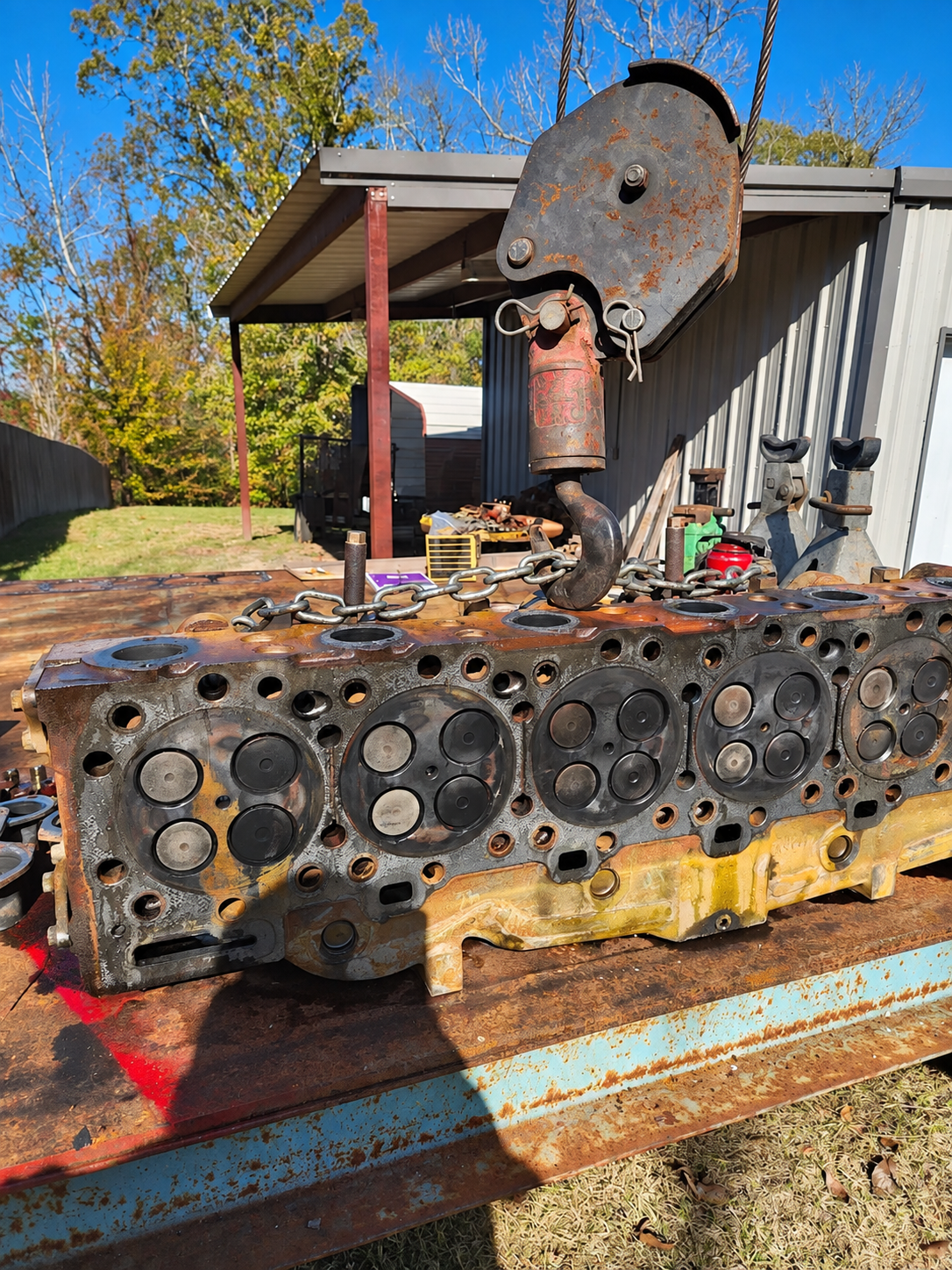 Removed cylinder head on a work surface, with valves visible and a hoist hook above.