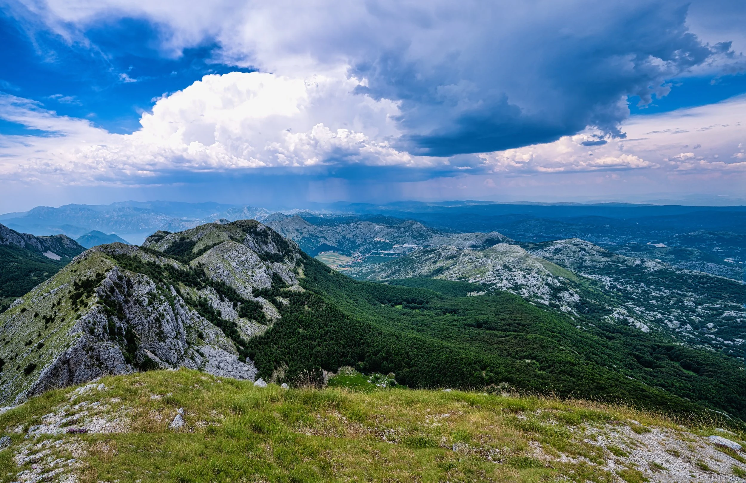 A panoramic view of a mountain range with rocky peaks covered in greenery and a partly cloudy sky overhead.