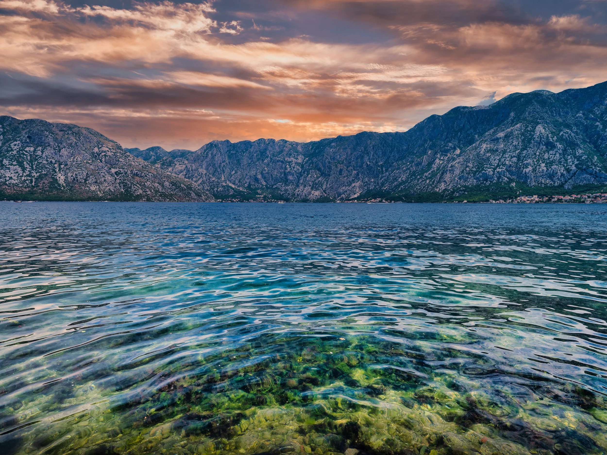 Scenic view of a lake with mountain range in the background during sunset, with colorful clouds in the sky.