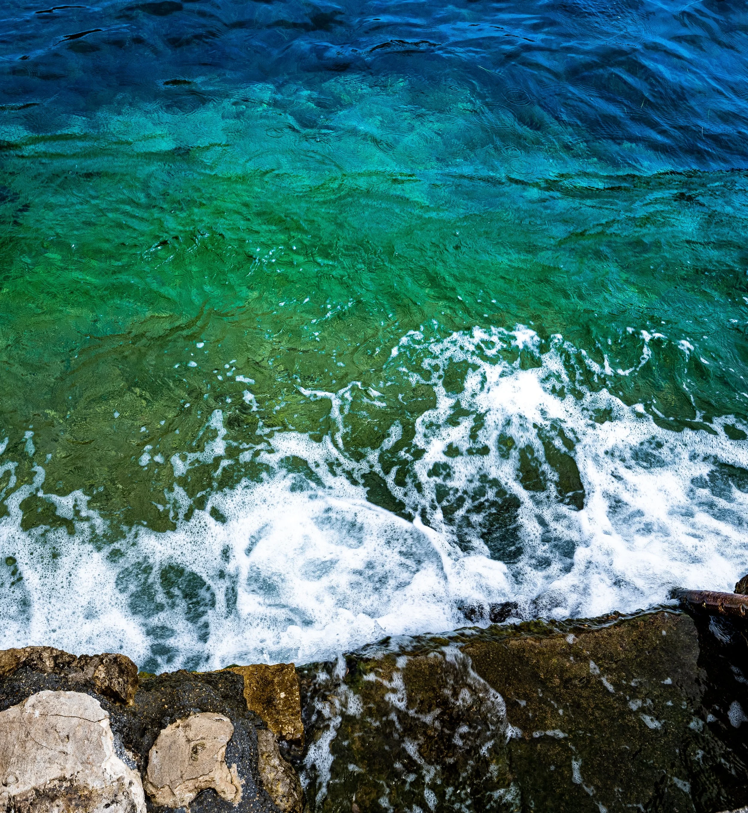 Waterfront with rocks at the shore, waves crashing, and murky water in the ocean.