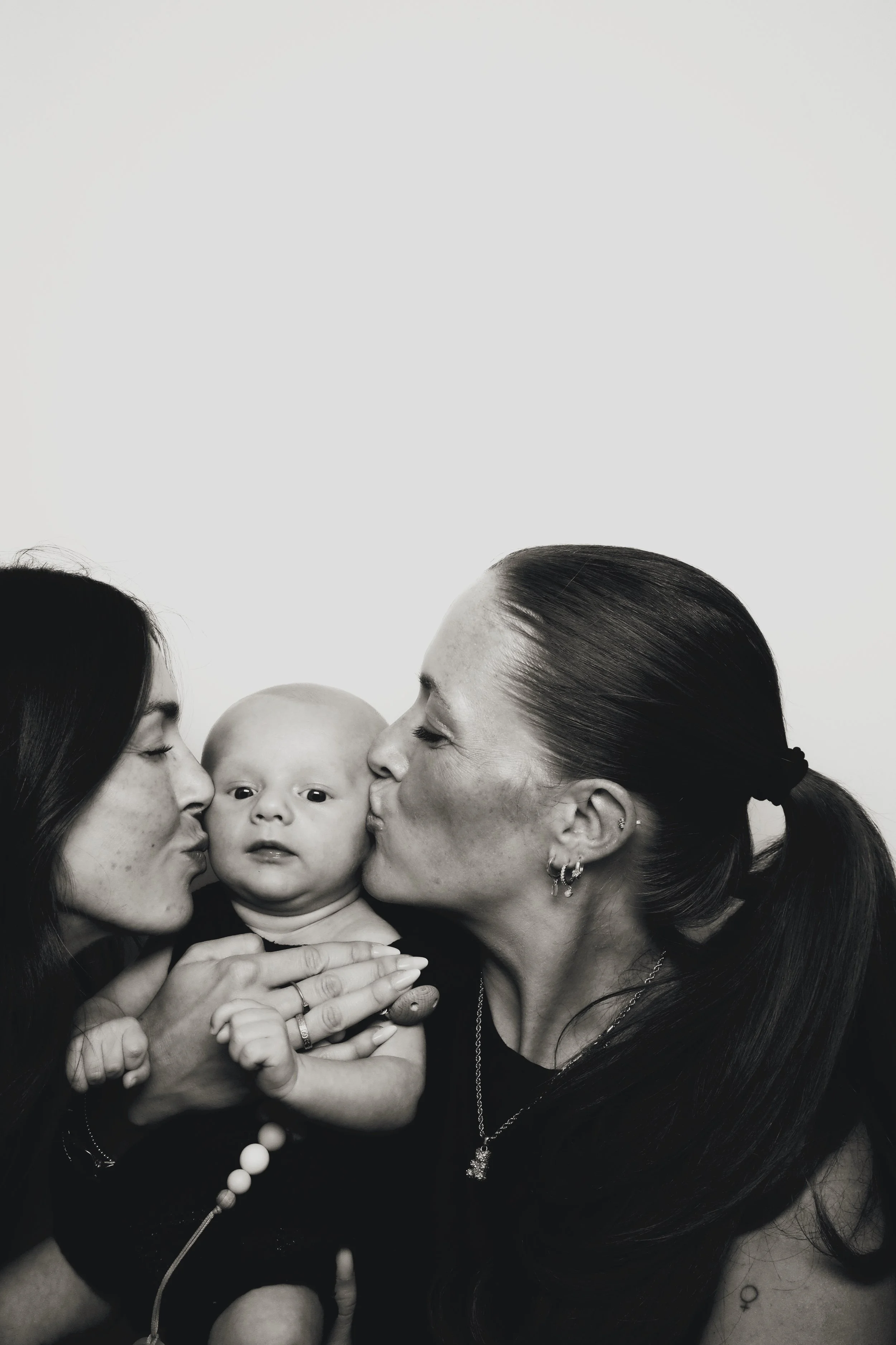 Family photo strip from 801 Booth showing two women kissing a baby on each cheek