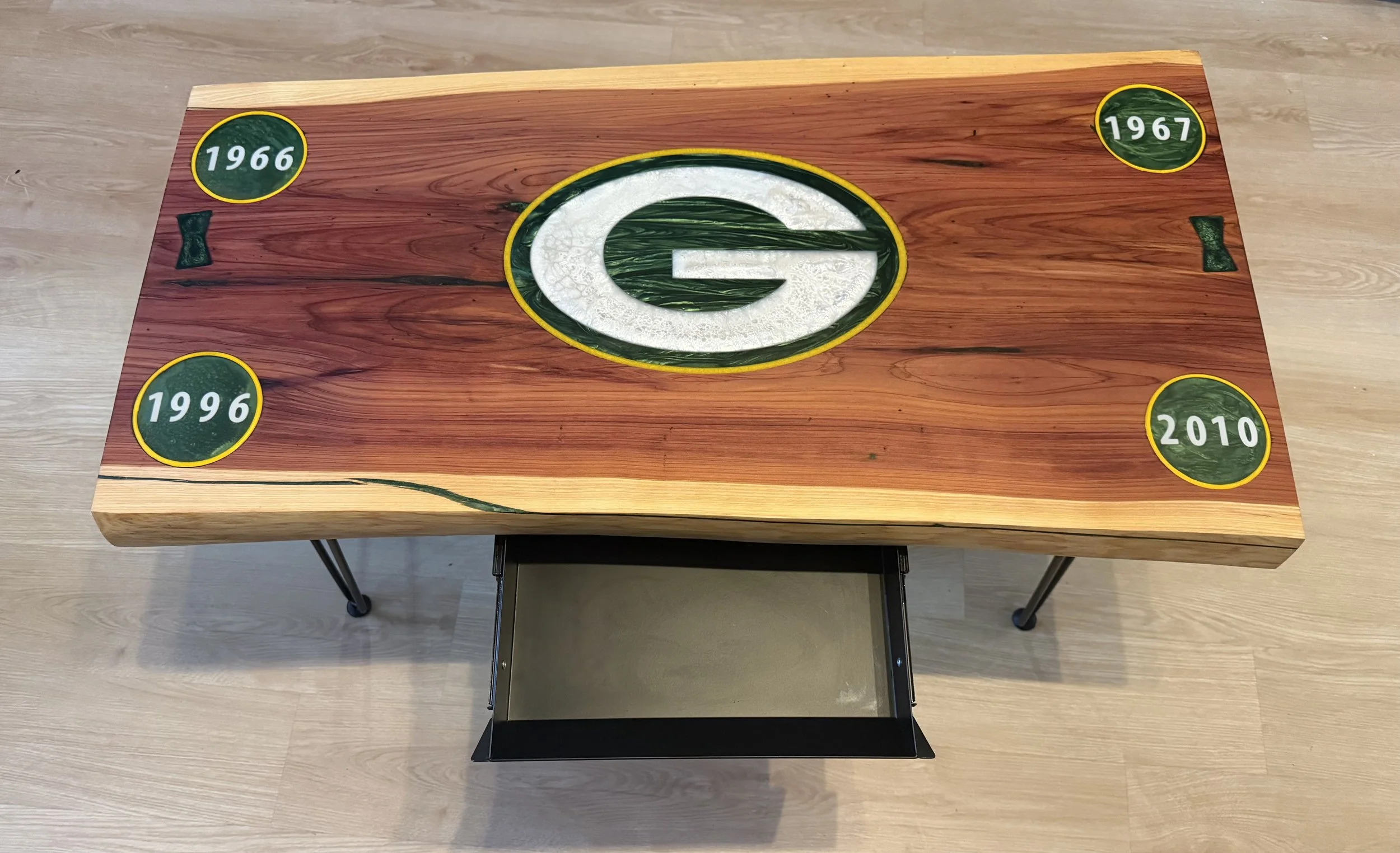 Wooden table featuring a green and white Green Bay Packers logo in the center and four patches with years 1966, 1967, 1996, and 2010 on each corner.