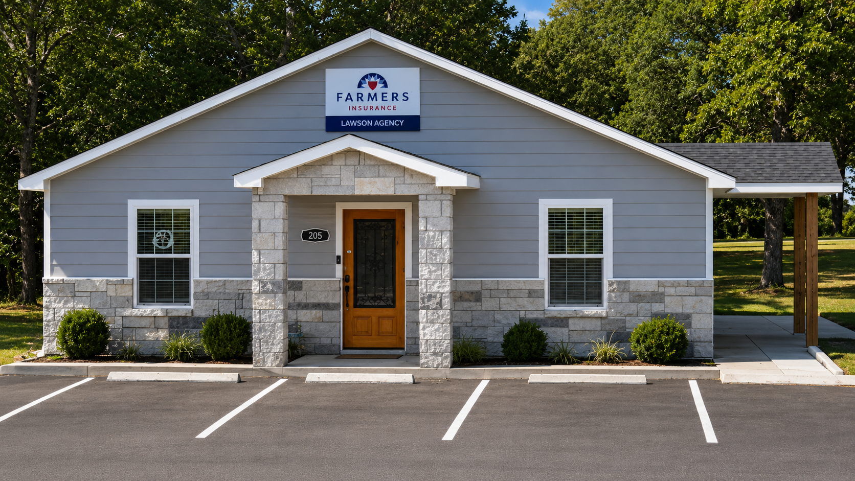 Single-story office building with grey siding, stone accents, and a wooden door, labeled Farmers Insurance Lawson Agency, with a small parking lot in the front and trees in the background.