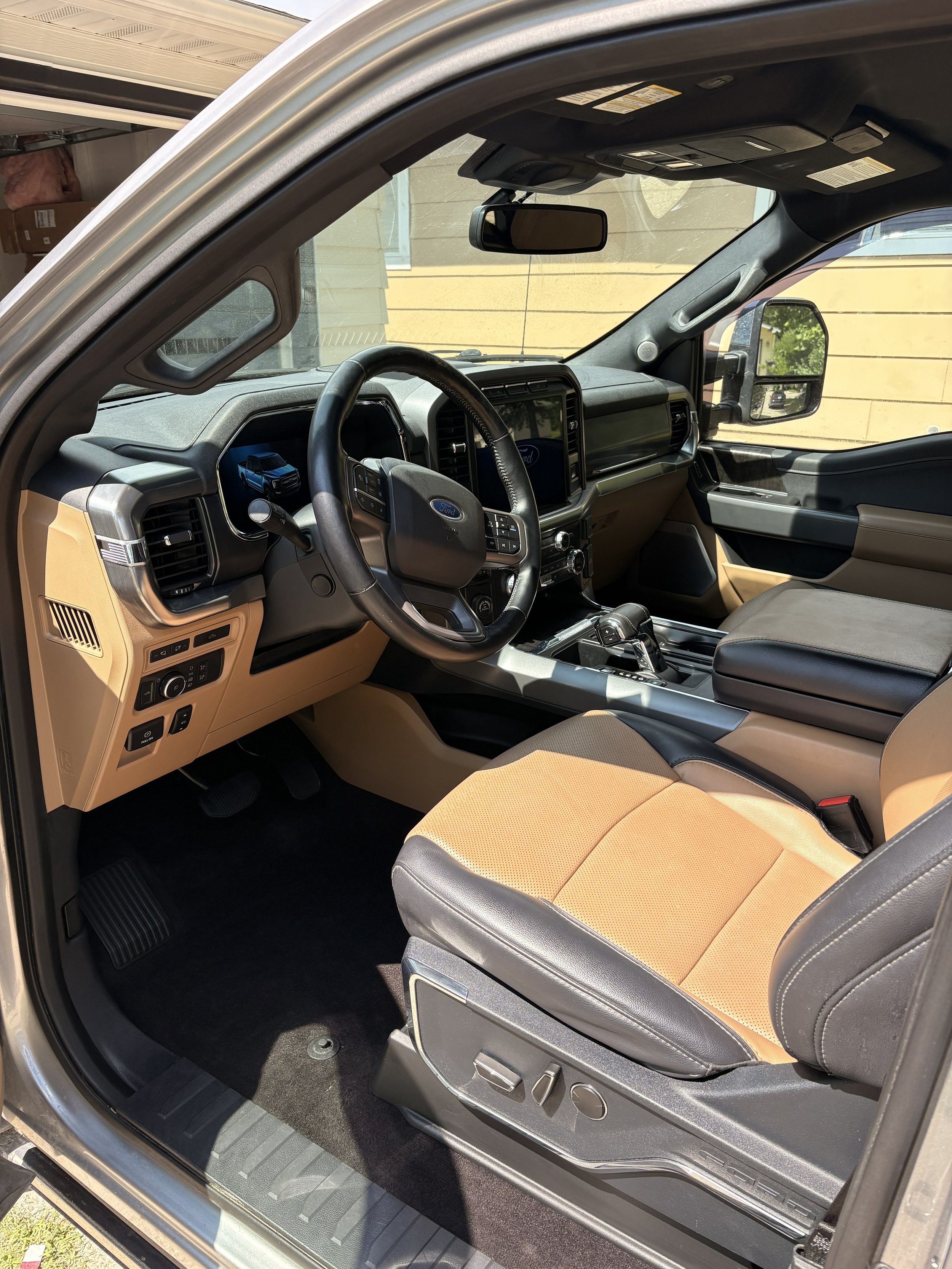 The image shows the interior of a modern Ford vehicle, focusing on the driver's seat and dashboard area, with a view of the steering wheel, center console, and passenger seat.