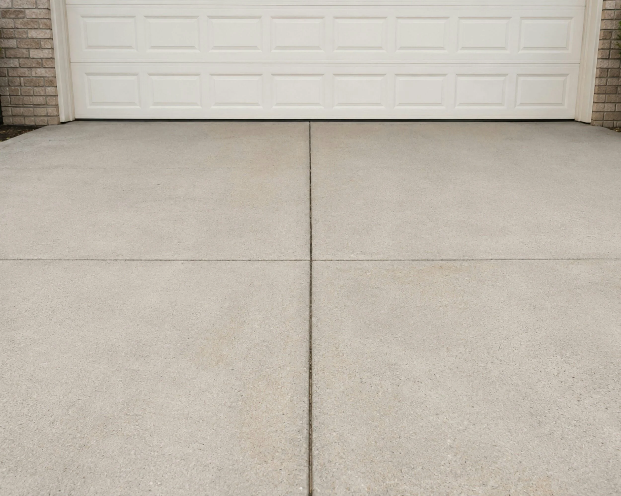 A white garage door with a brick wall on each side, and concrete driveway in front.