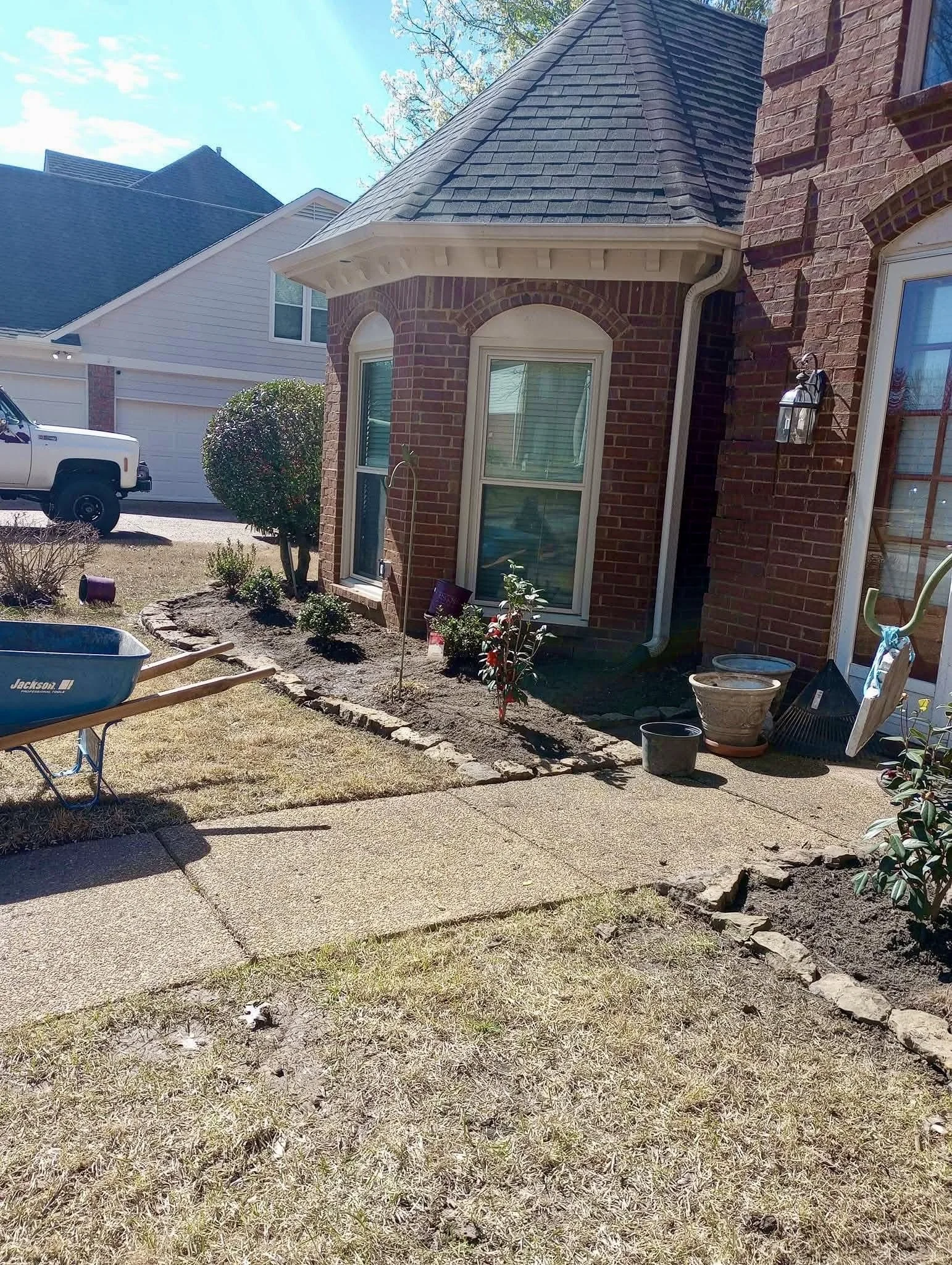 Backyard with patio, small trees, flower pots, and a house with brick exterior and large window.