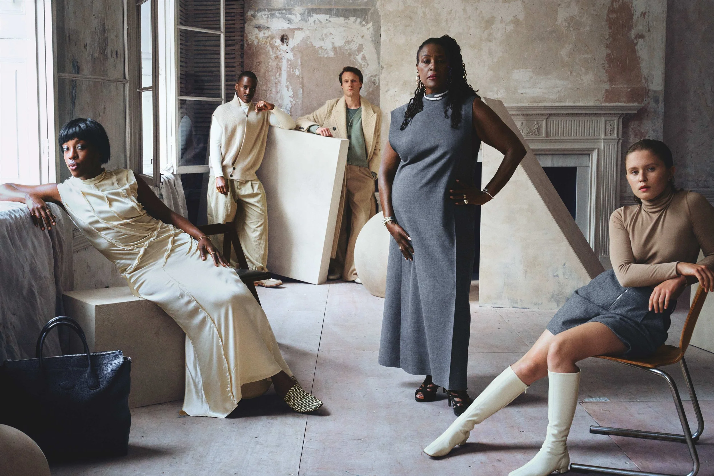 Group of five diverse women in stylish clothing posing in an art studio with a rustic interior, some sitting and others standing, surrounded by art supplies and artwork.