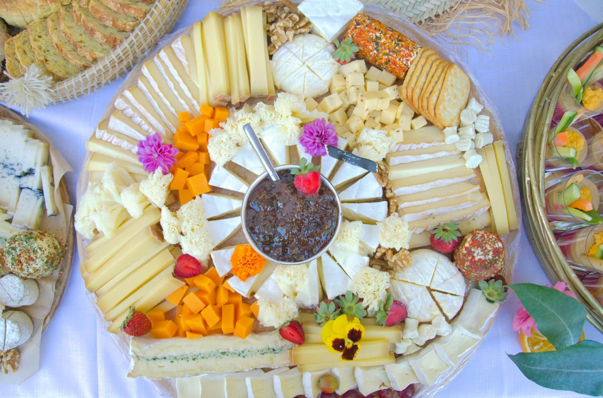 Plate de fromages variés accompagnée de fruits frais, confiture, et crackers, décorée de fleurs.