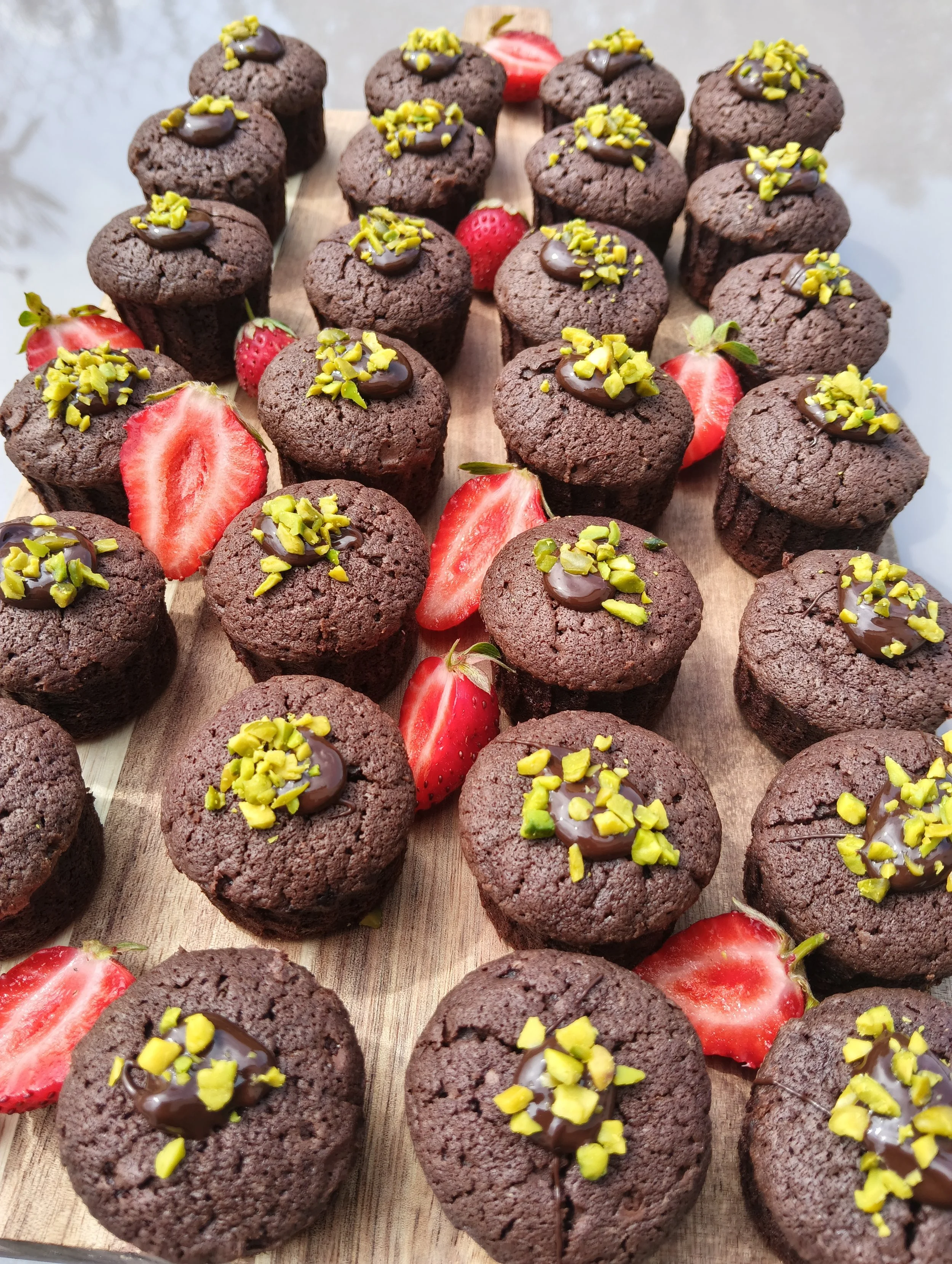 Gros plans de cupcakes au chocolat garnis de noix de pistache hachée, avec des fraises fraîches en décoration, sur une planche en bois.