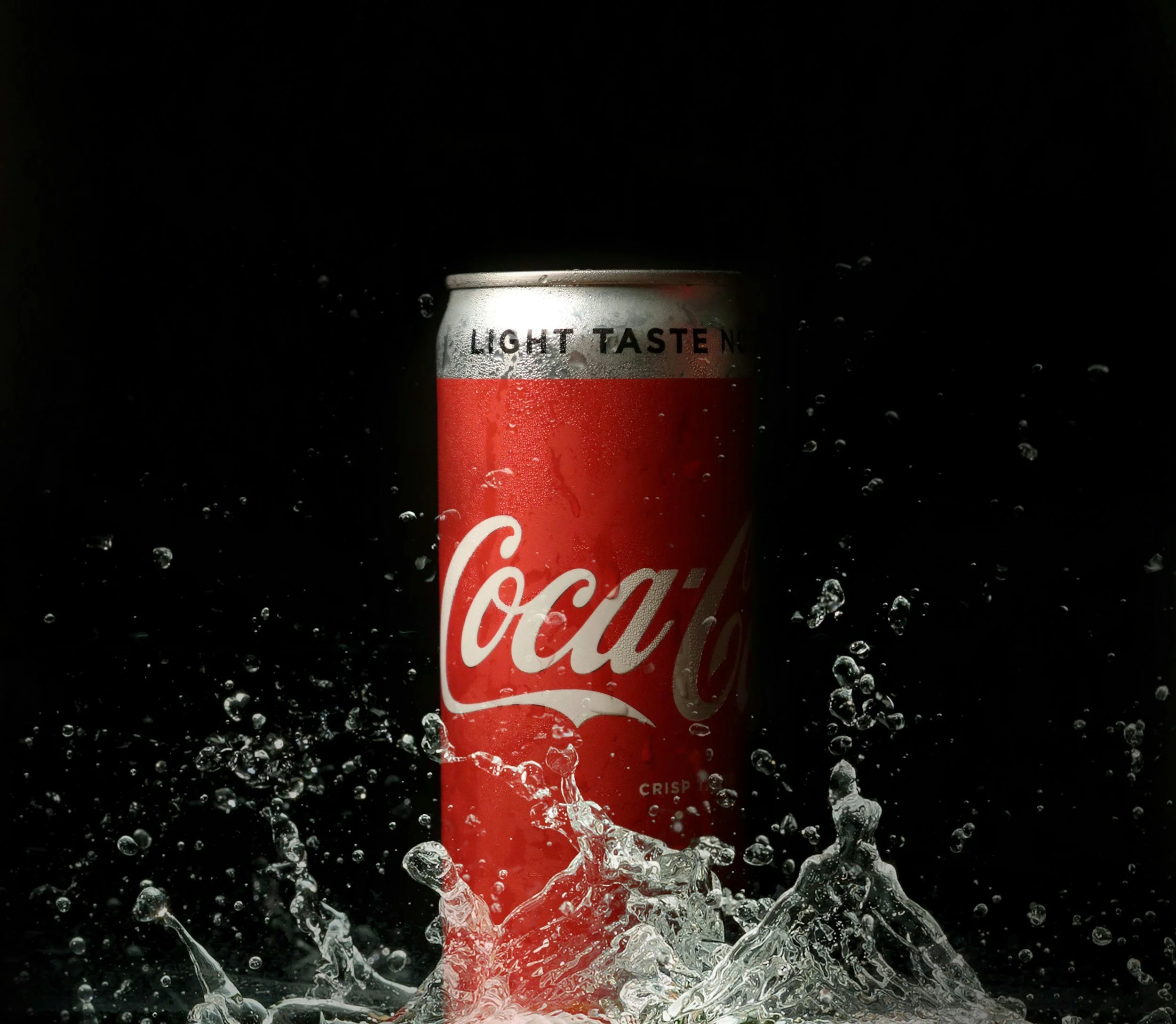 A can of Coca-Cola soda with water splashing around it, condensation on the can, and a dark background.