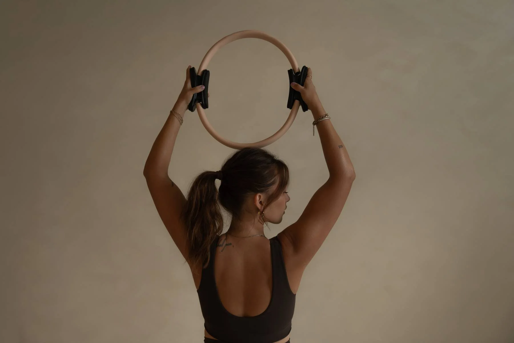 Woman holding a fitness ring above her head with both hands, facing sideways, dark background