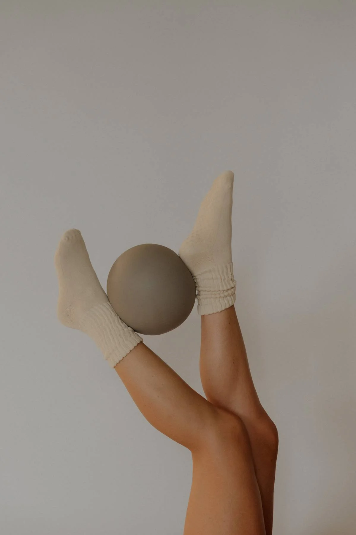 A person's arm with a beige sock on the hand, holding a gray sphere. The background is plain and light-colored.