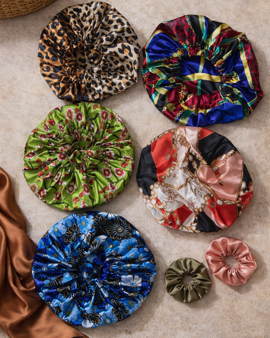 Five colorful satin scrunchies with various patterns and colors, placed on a beige surface, with additional satin fabric swatches nearby.