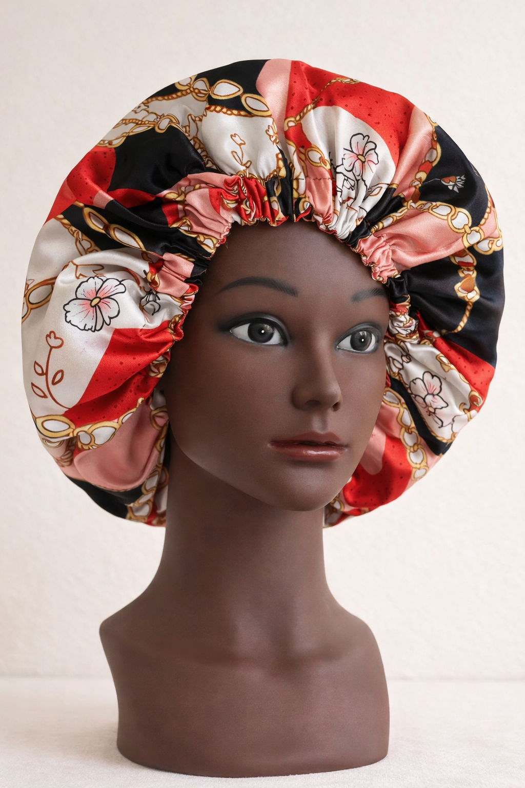 Mannequin head wearing a colorful silk bonnet with floral and chain patterns.