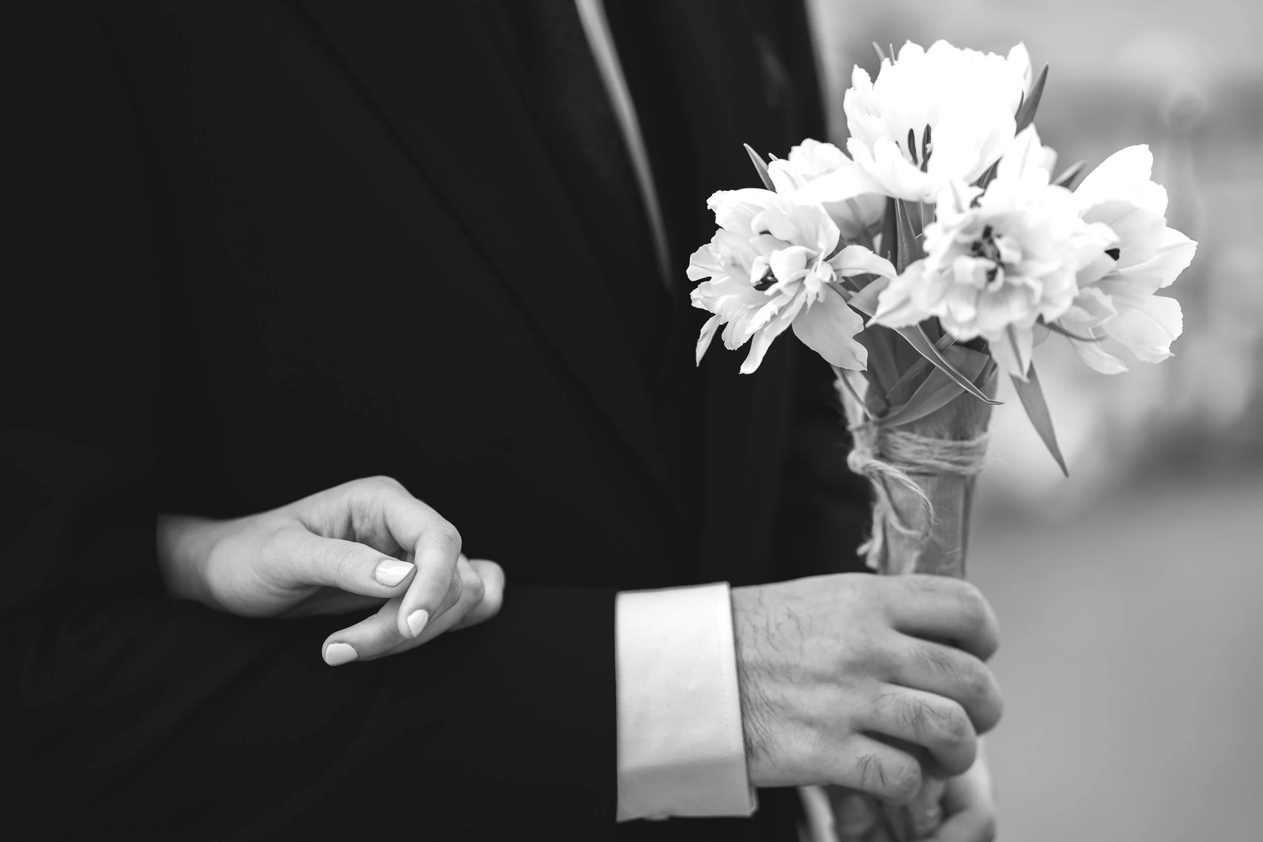 A black and white photo of a person in a suit holding a bouquet of flowers, with a small card in their hand.